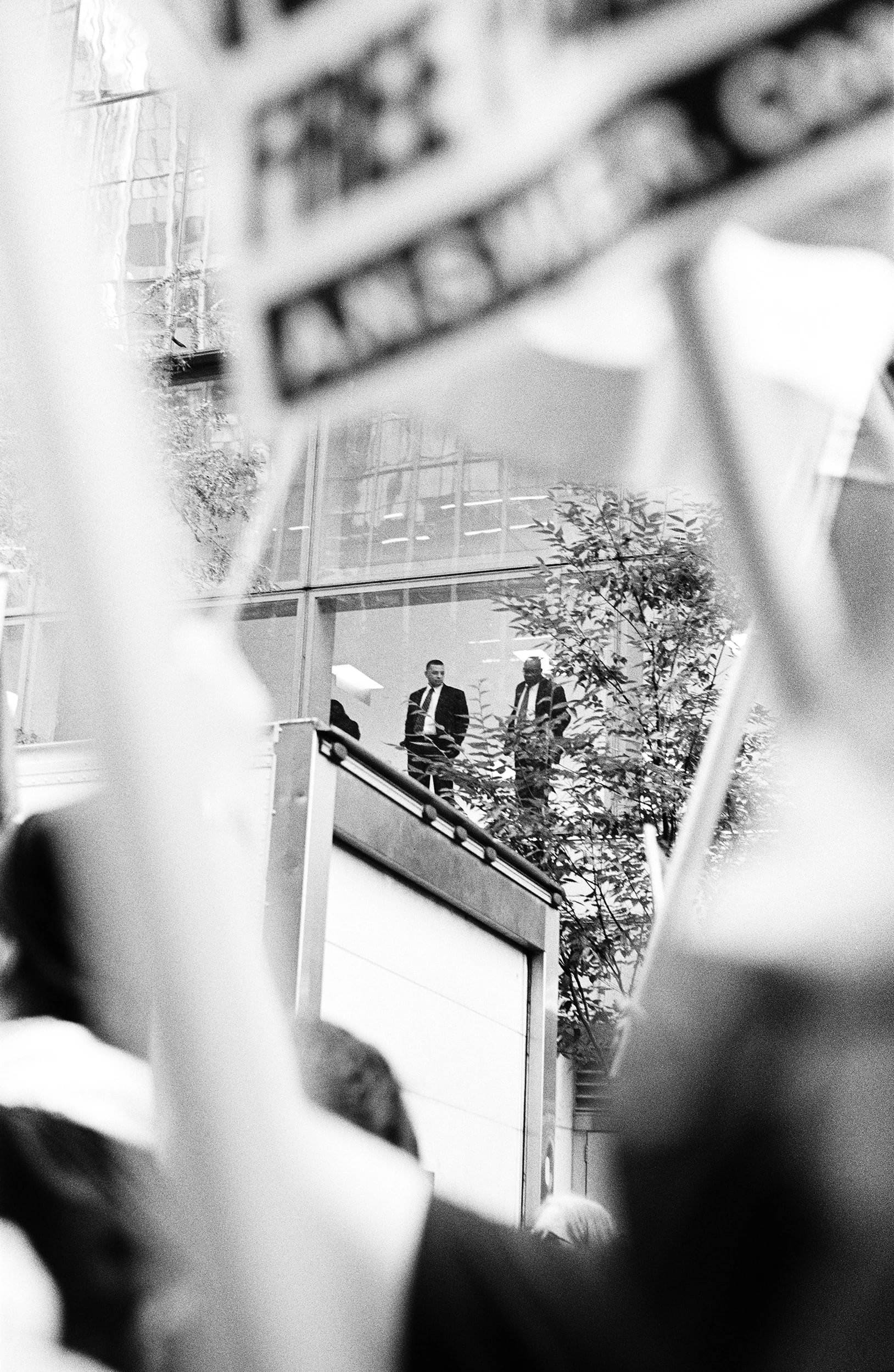 Two men in suits observe a protest from an elevated position