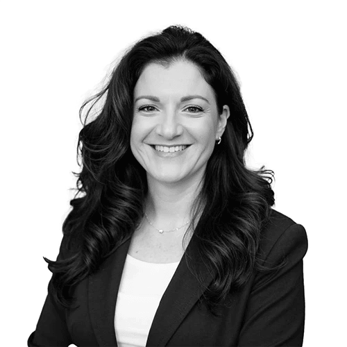 A monochrome image cropped to below the shoulders of a woman with dark brown hair, a white shirt, and black blazer.