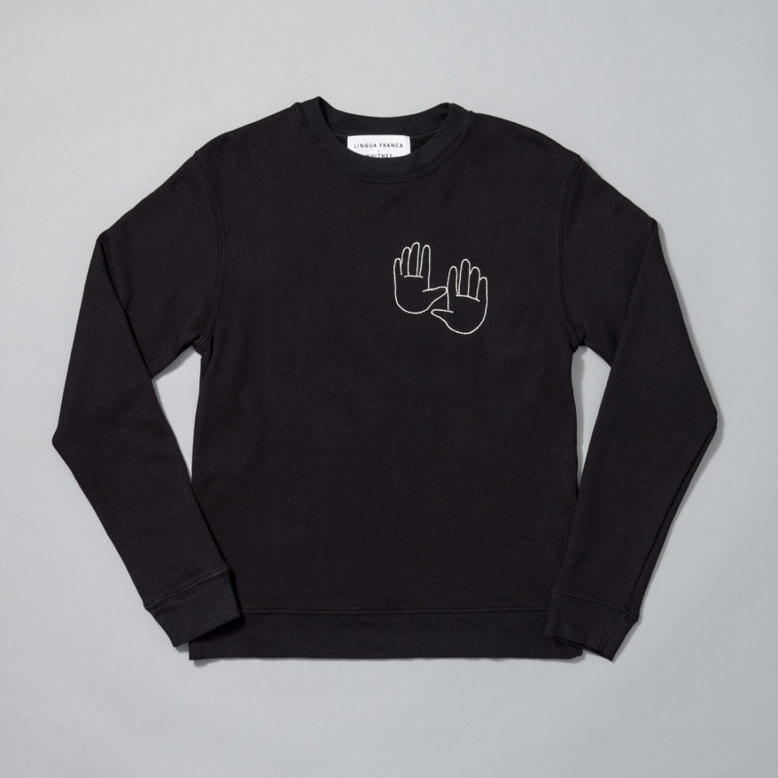 A photograph of a black crew neck with two hands printed on the left side of the crew neck.