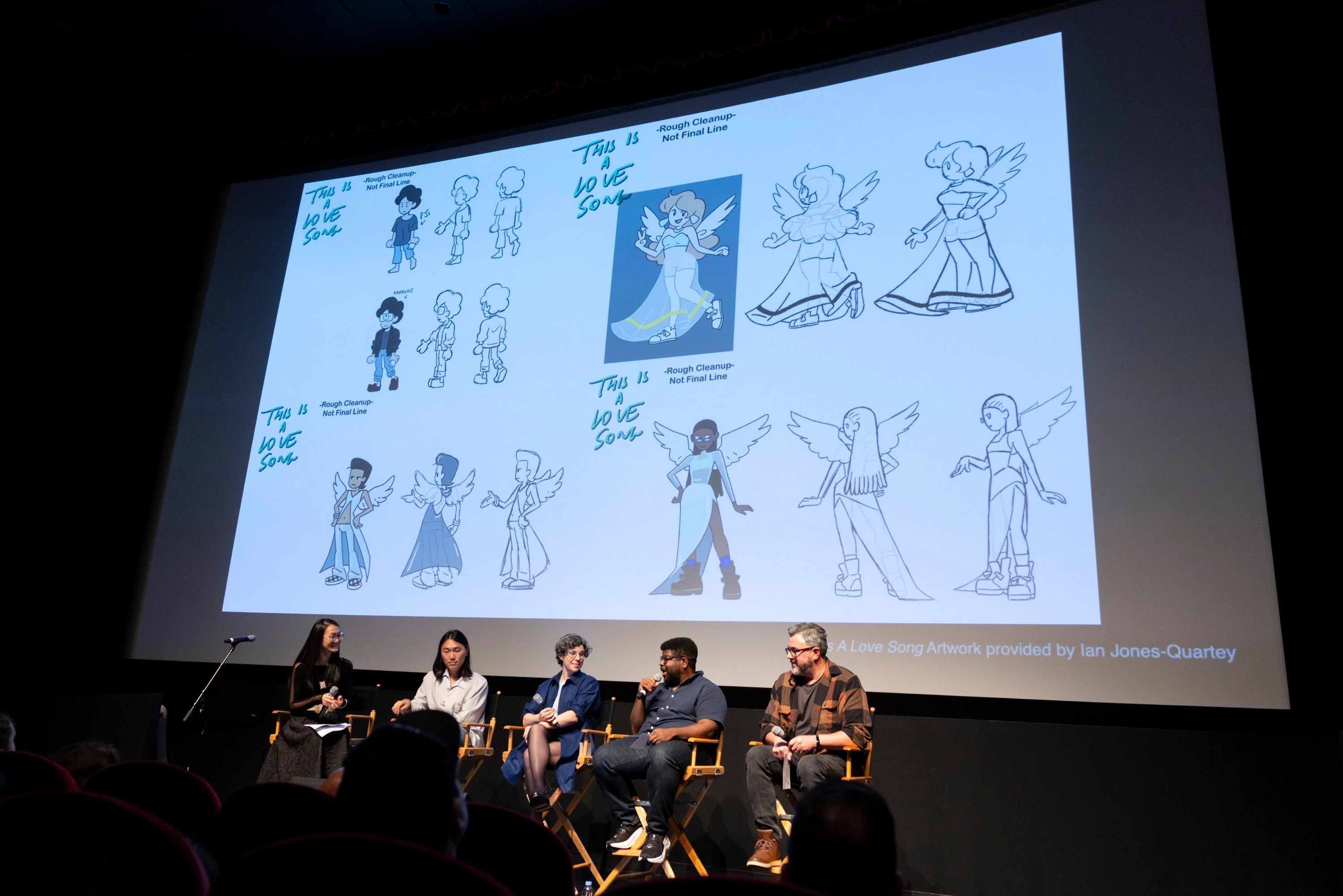 Five individuals sitting on stage with a slide displaying artwork by Ian Jones-Quartey from This is a Love Song in the background.