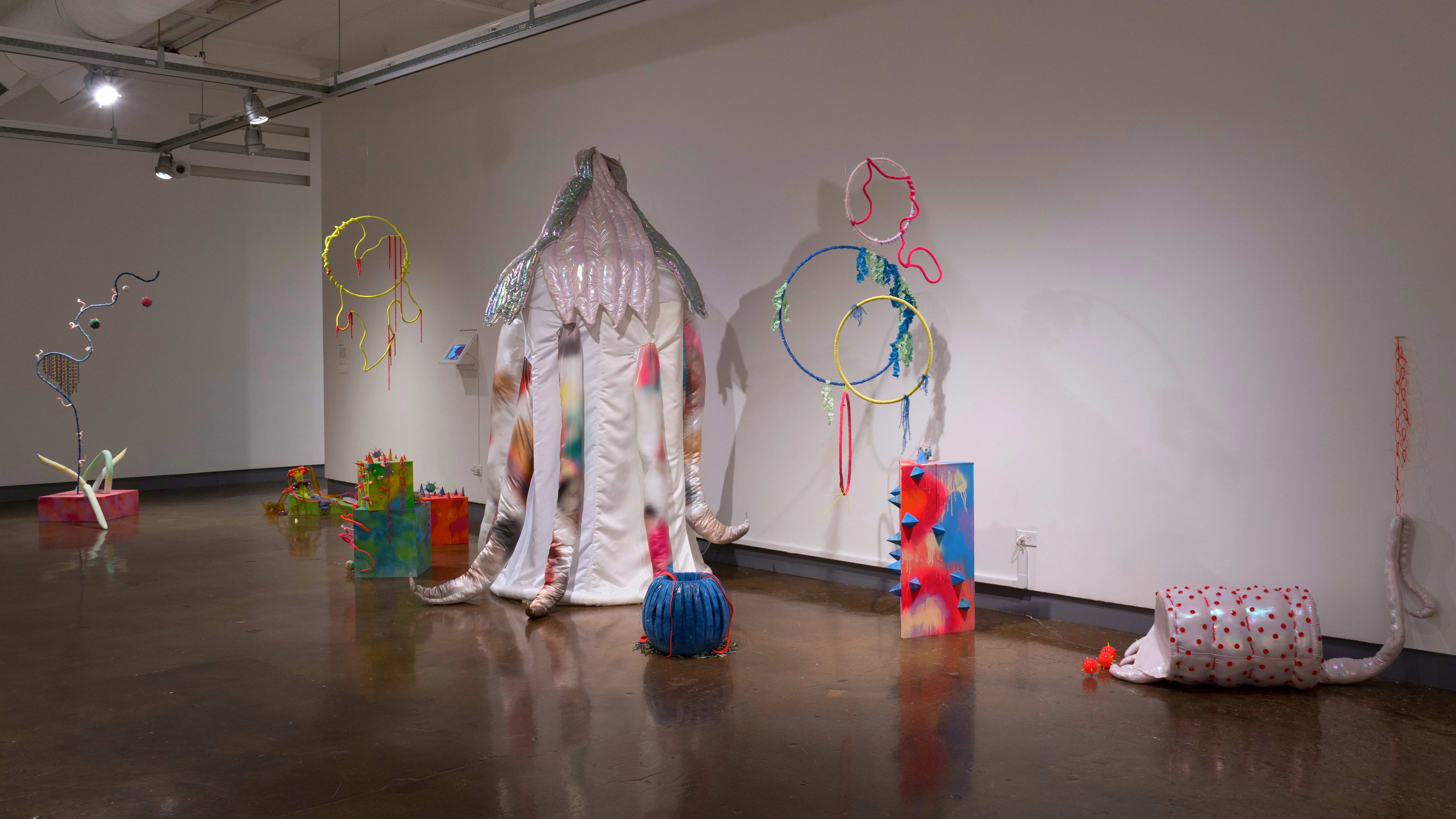 Multiple abstract sculptures are placed on the floor or hang from the ceiling. They're made up of a lot of loopy shapes and bright colors.