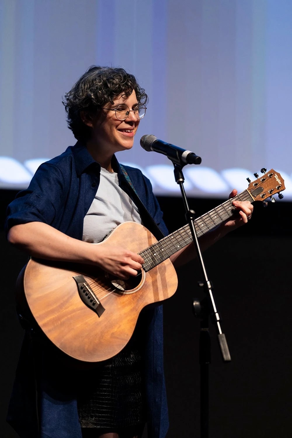 An individual hold an acoustic guitar standing on stage.