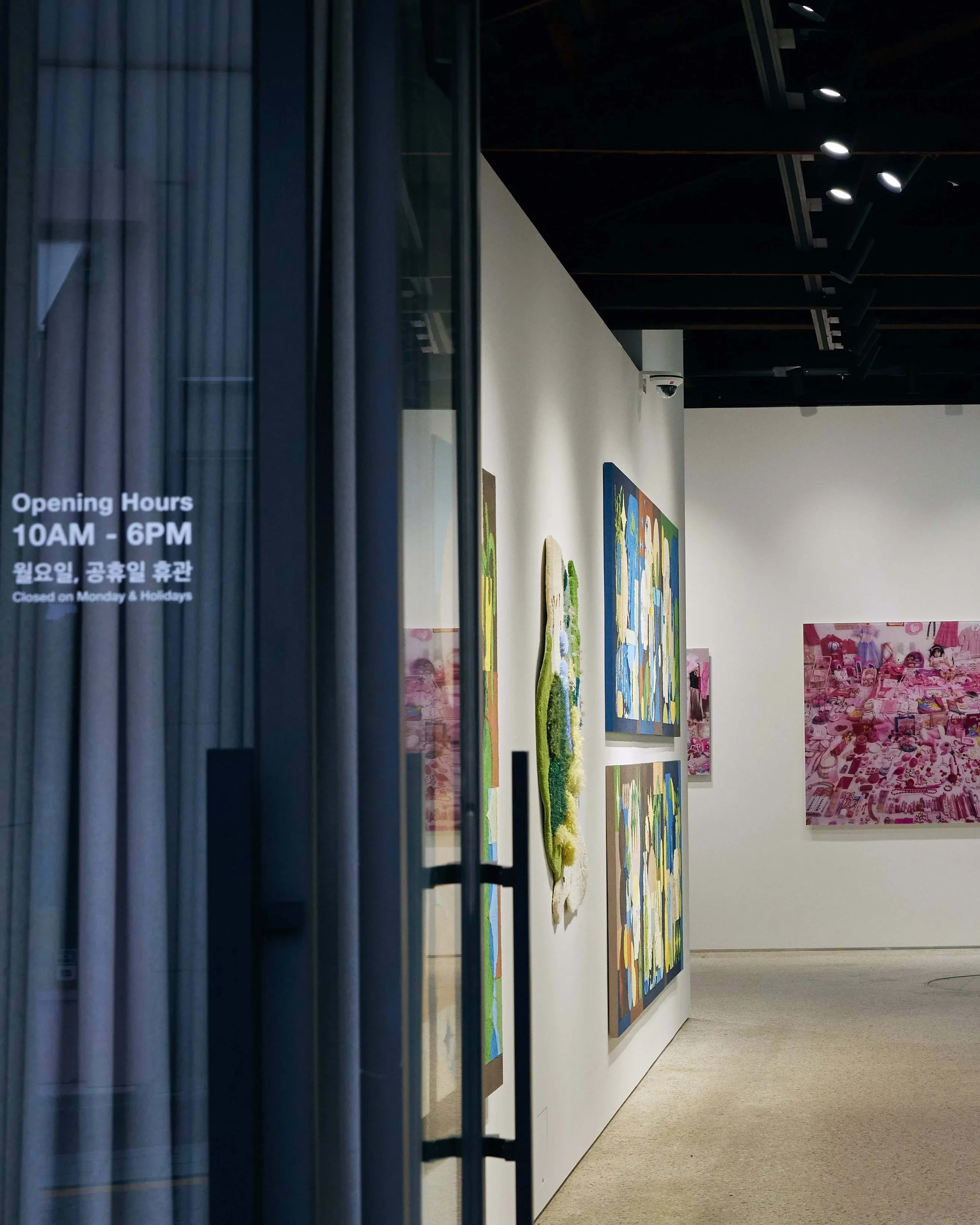 Doors propped open at a gallery's facade, revealing an in-progress exhibition with many art pieces hanging from the three visible walls.