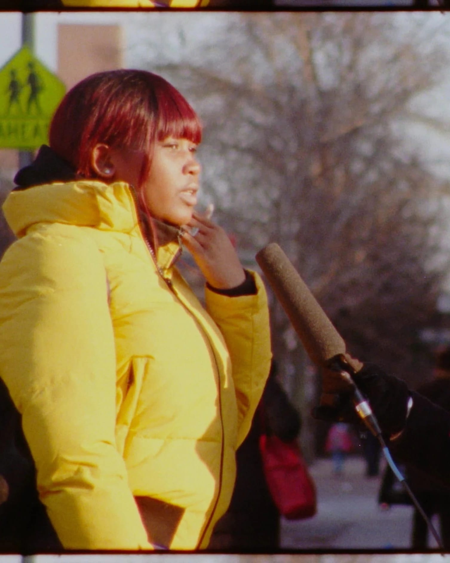 Video still of a woman interviewing another woman on the street. The interviewer hold a large microphone up.