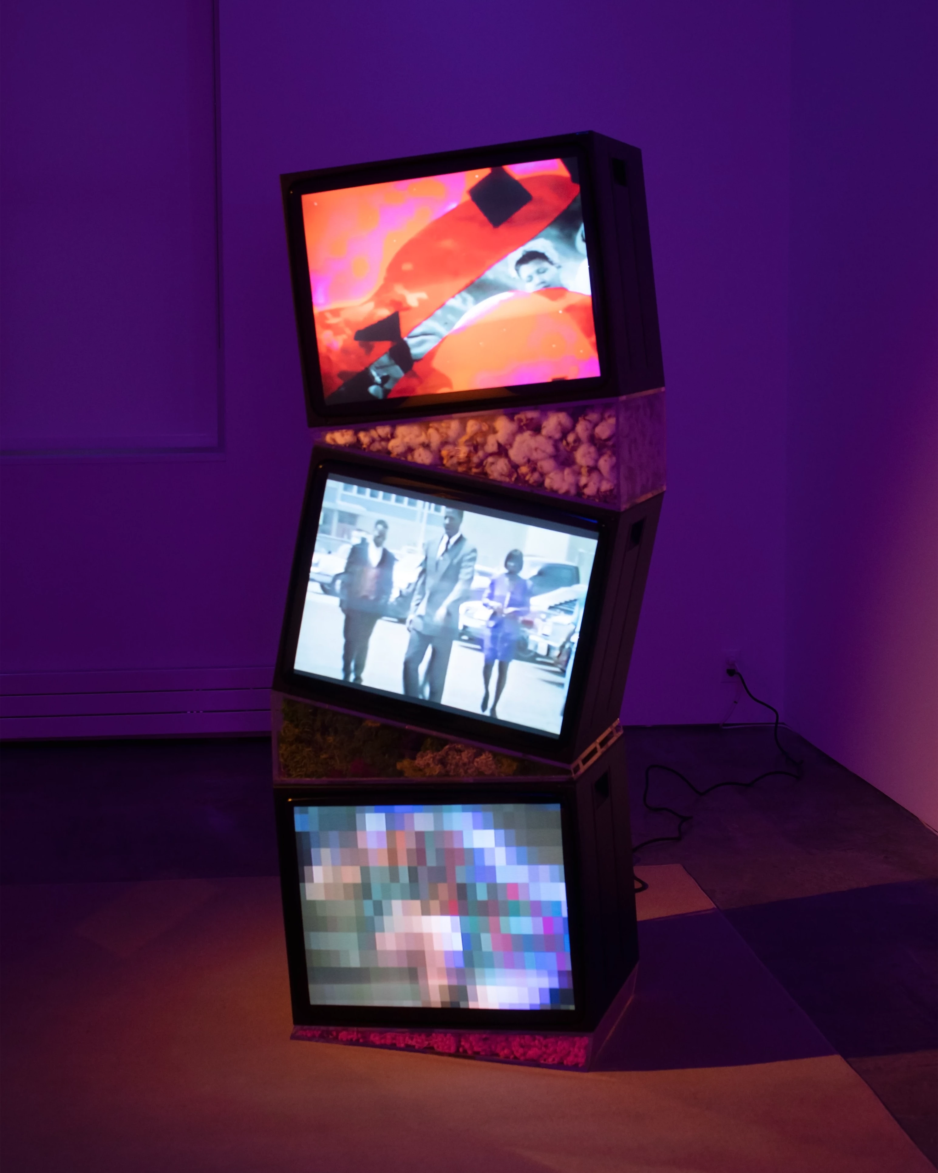 Picture of a museum installation with three old televisions stacked on top of each other, with different videos playing on each of them.