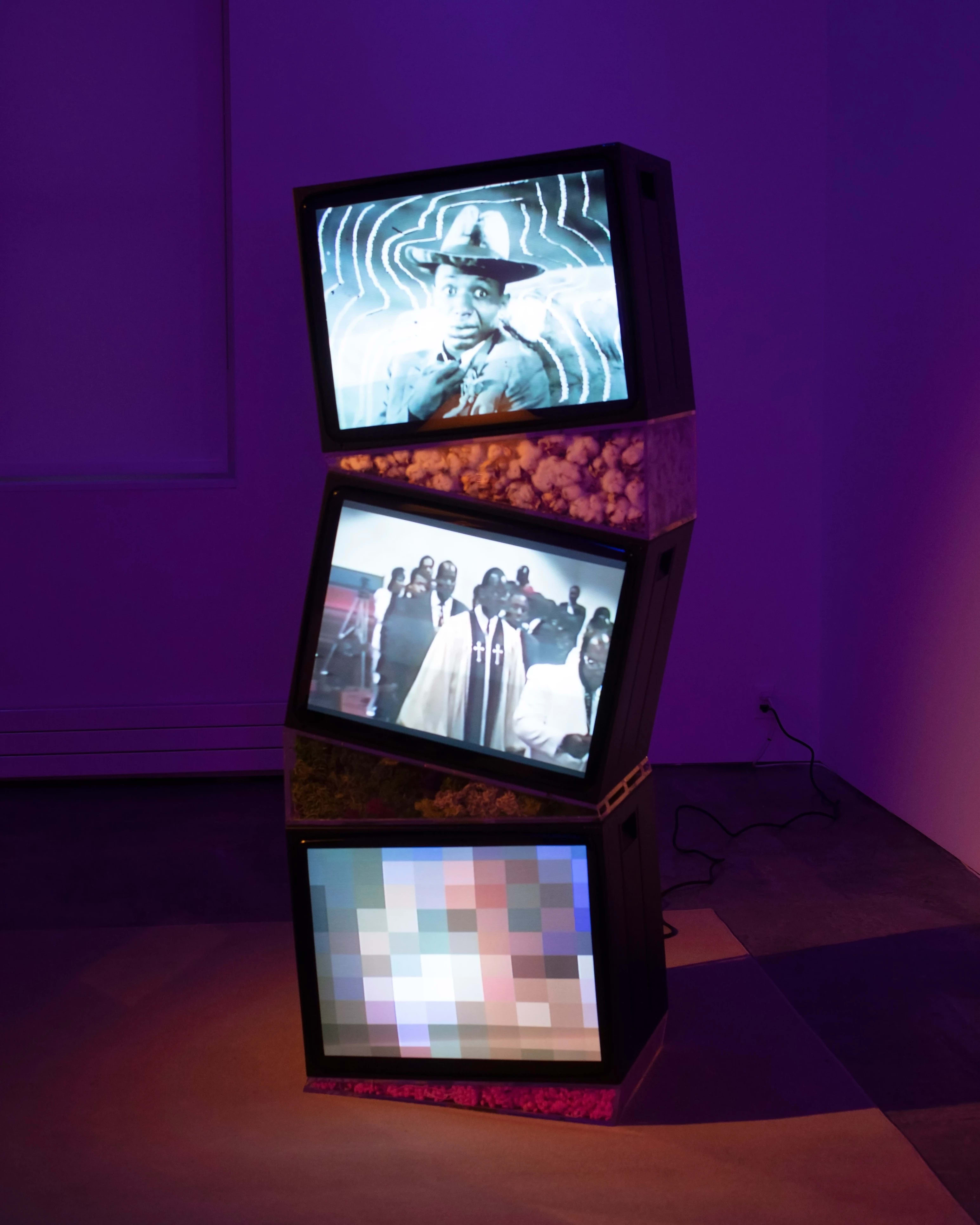 Picture of a museum installation with three old televisions stacked on top of each other, with different videos playing on each of them.