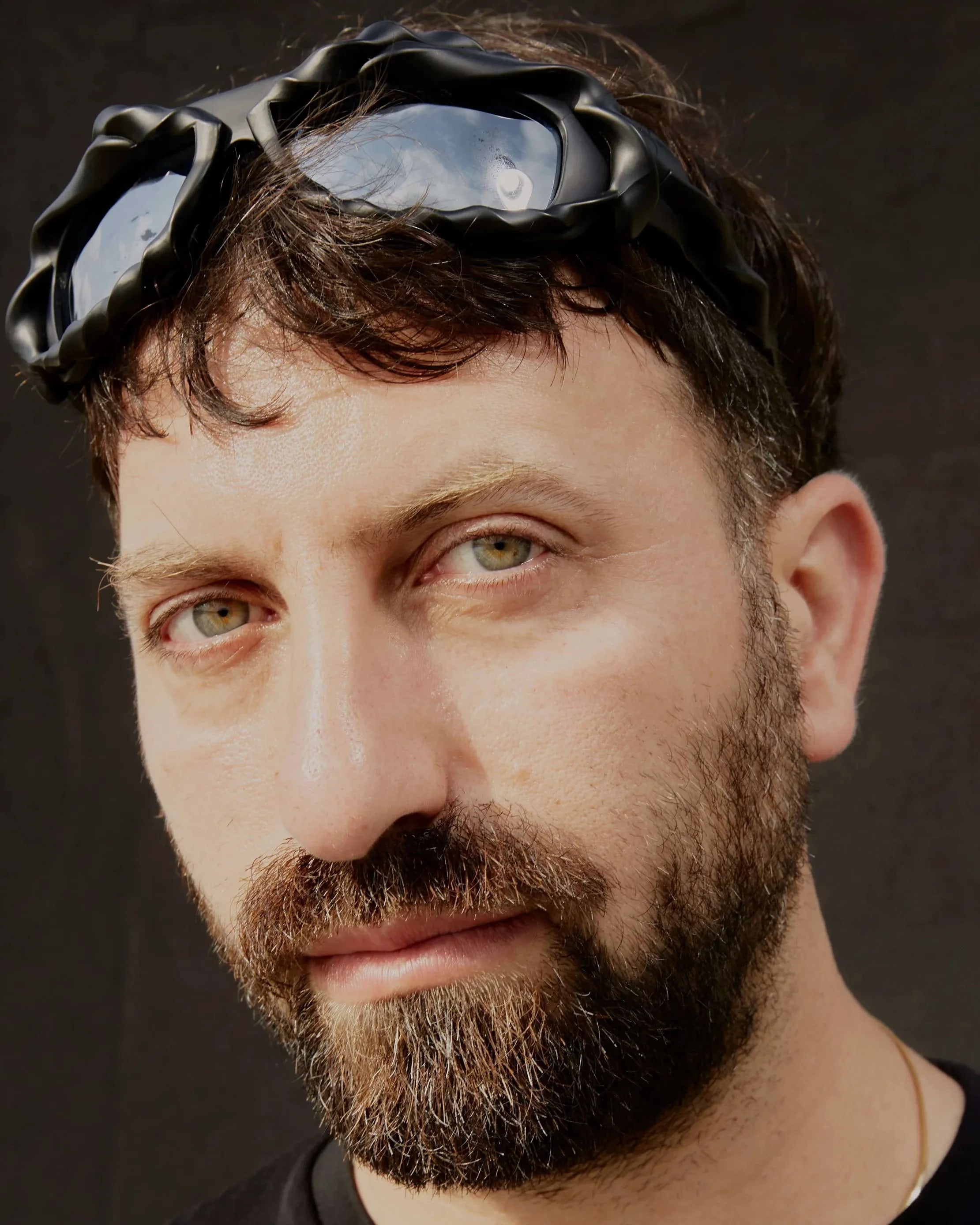 a person with a brown beard, bleached eyebrows and green eyes stares at the camera