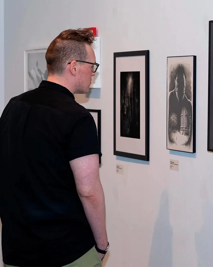 A man stands in front of a gallery wall, staring at a black and white piece.