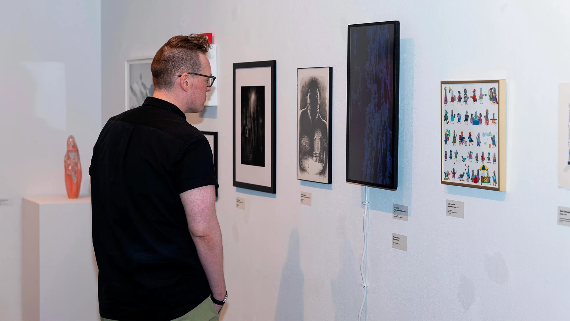 A man stands in front of a gallery wall, staring at a black and white piece.