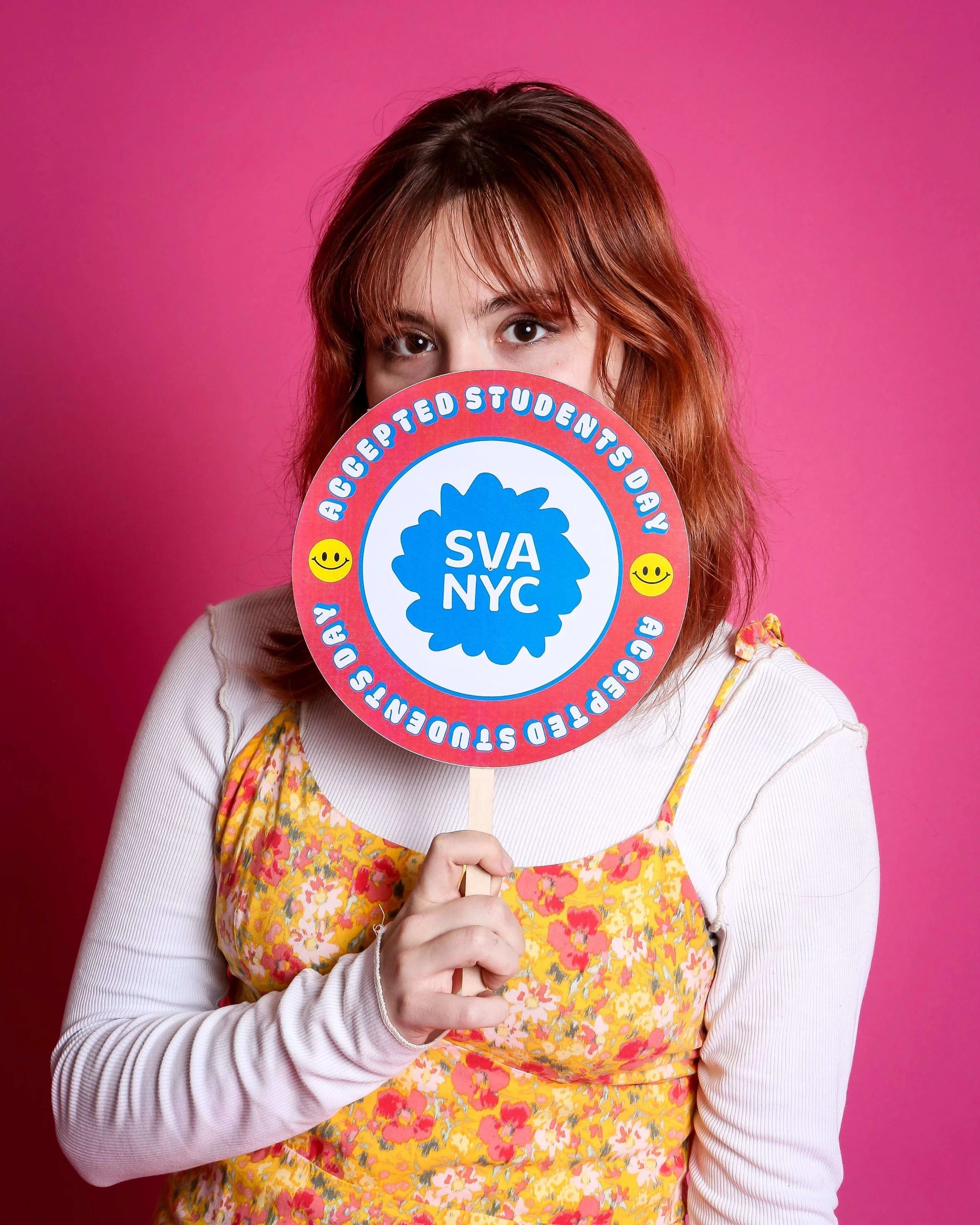 A person poses with a sign reading SVA NYC Accepted Students Day in front of a pink background