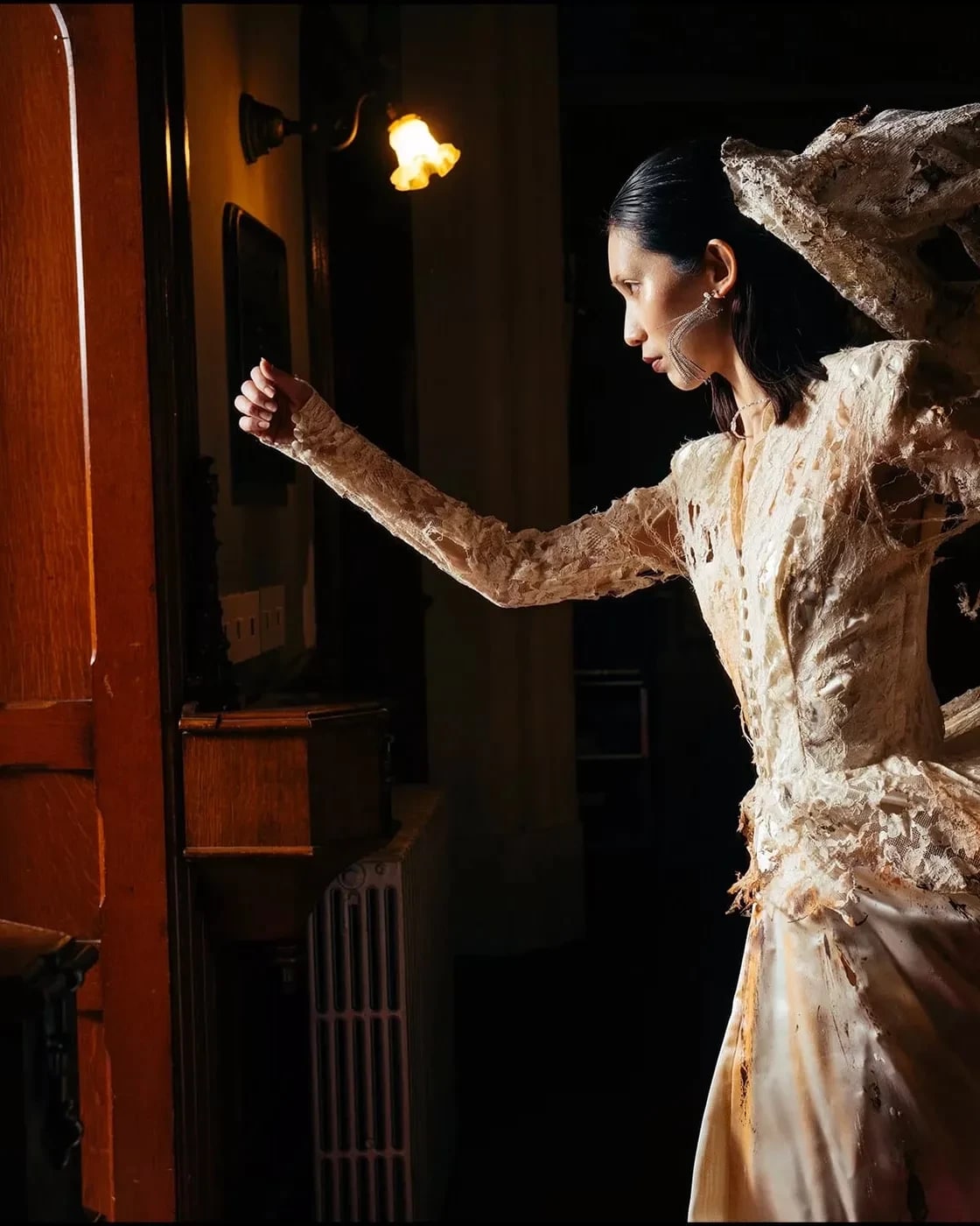 A woman in a burnt wedding dress runs out of a dimly lit building towards the door where light is coming through