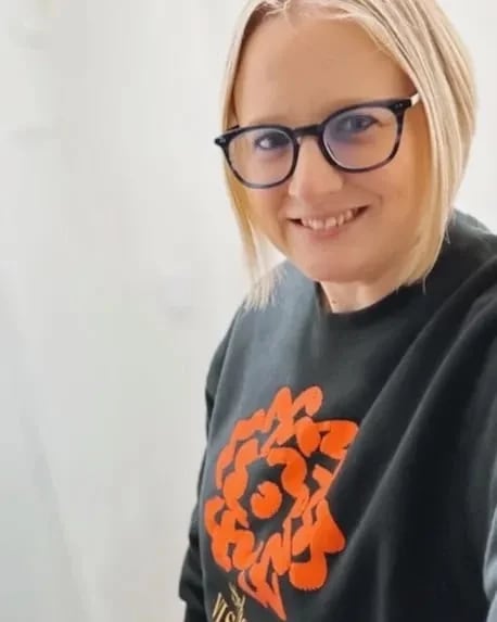 A woman with a short blonde bob and glasses smiles at the camera