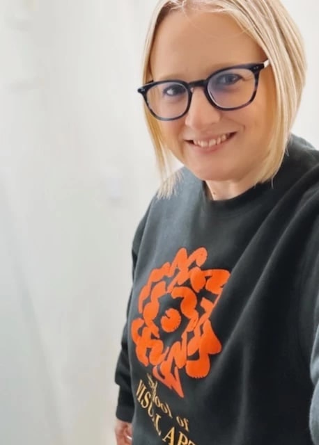 A woman with a short blonde bob and glasses smiles at the camera