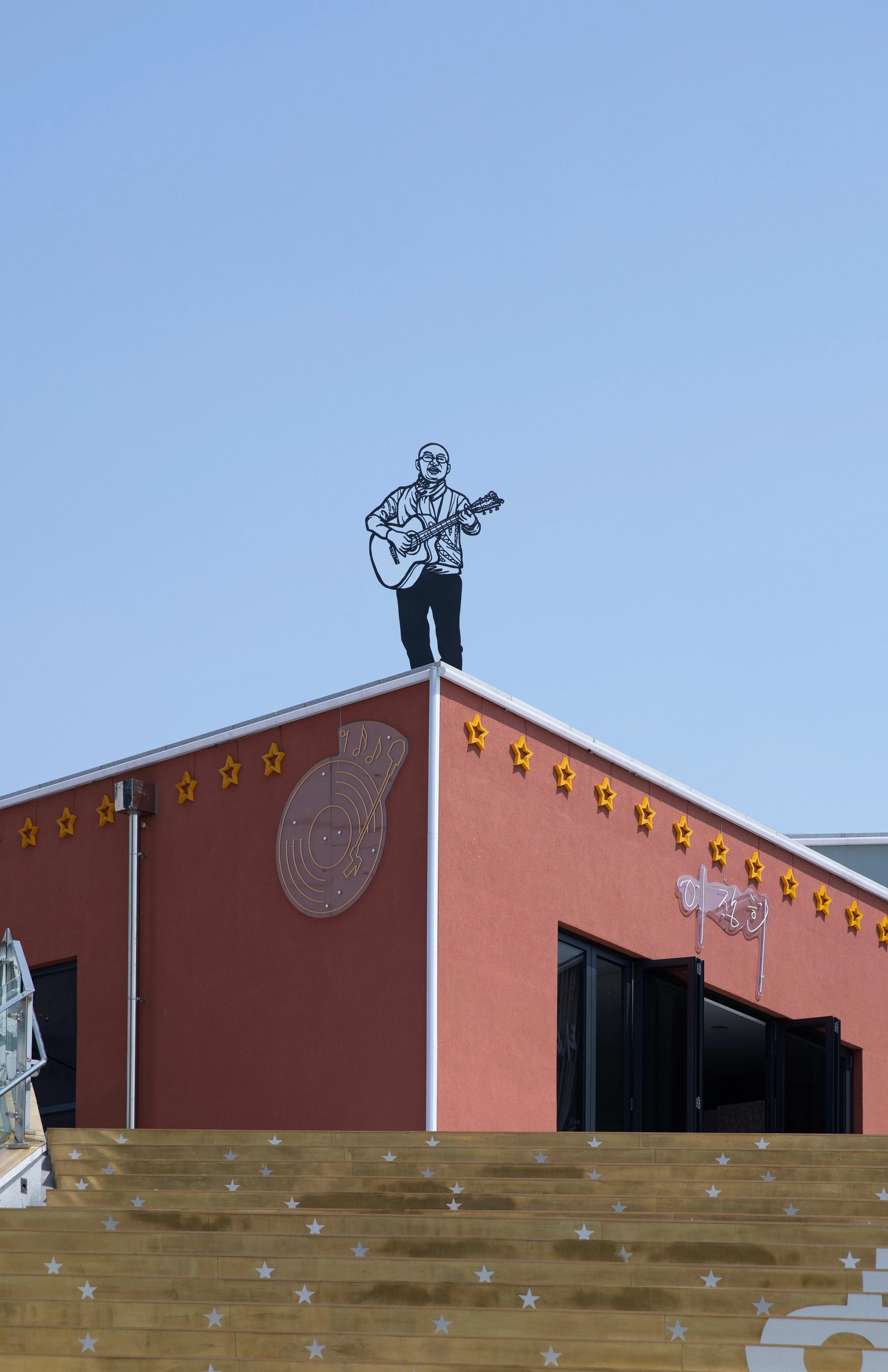 Sculpture made out of steel rods of a man playing guitar. Placed outside, on top of a short building.