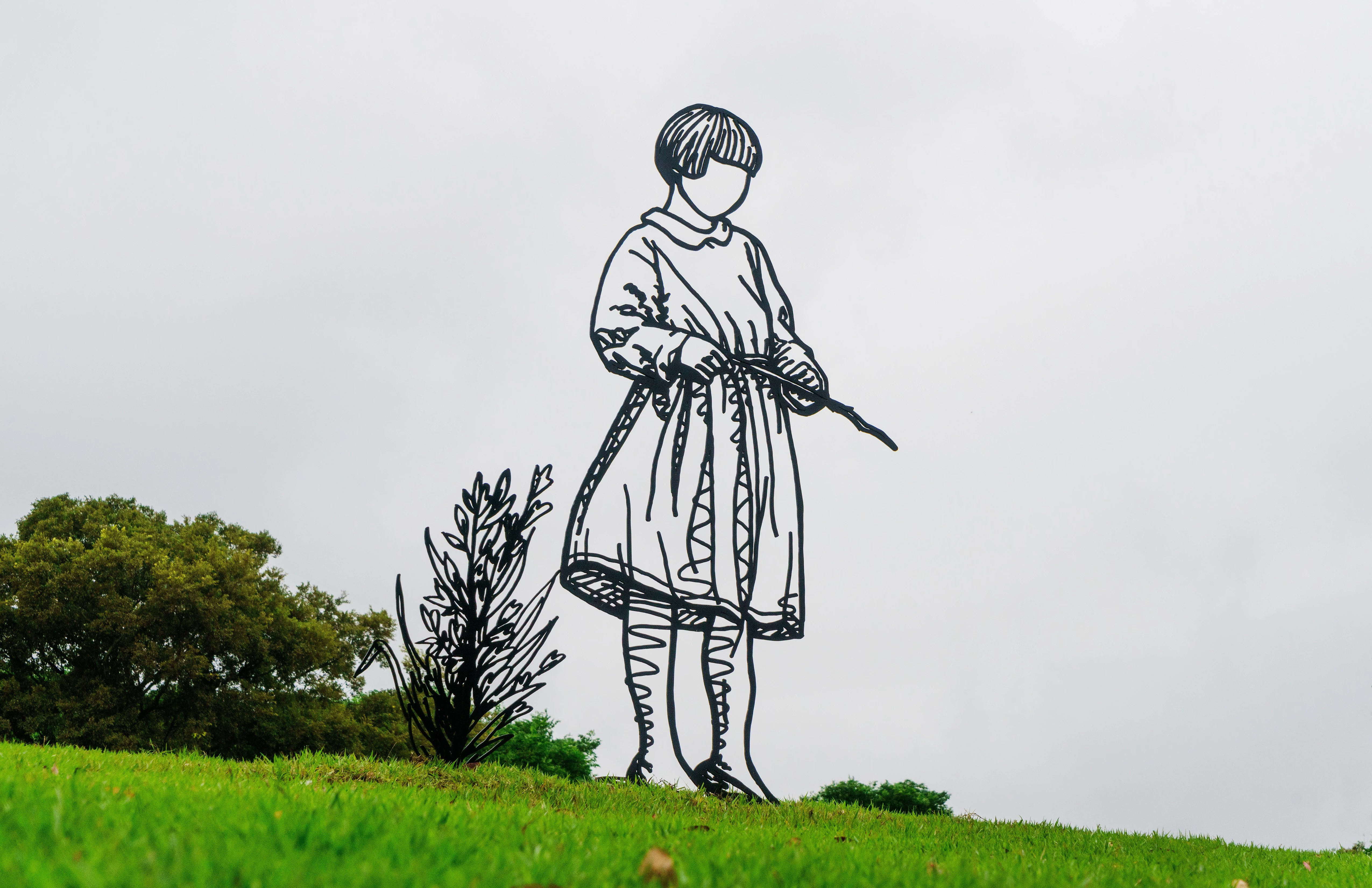 Sculpture made in steel rods on a little girl in a dress. The sculpture is set up outside, in a grassy place.