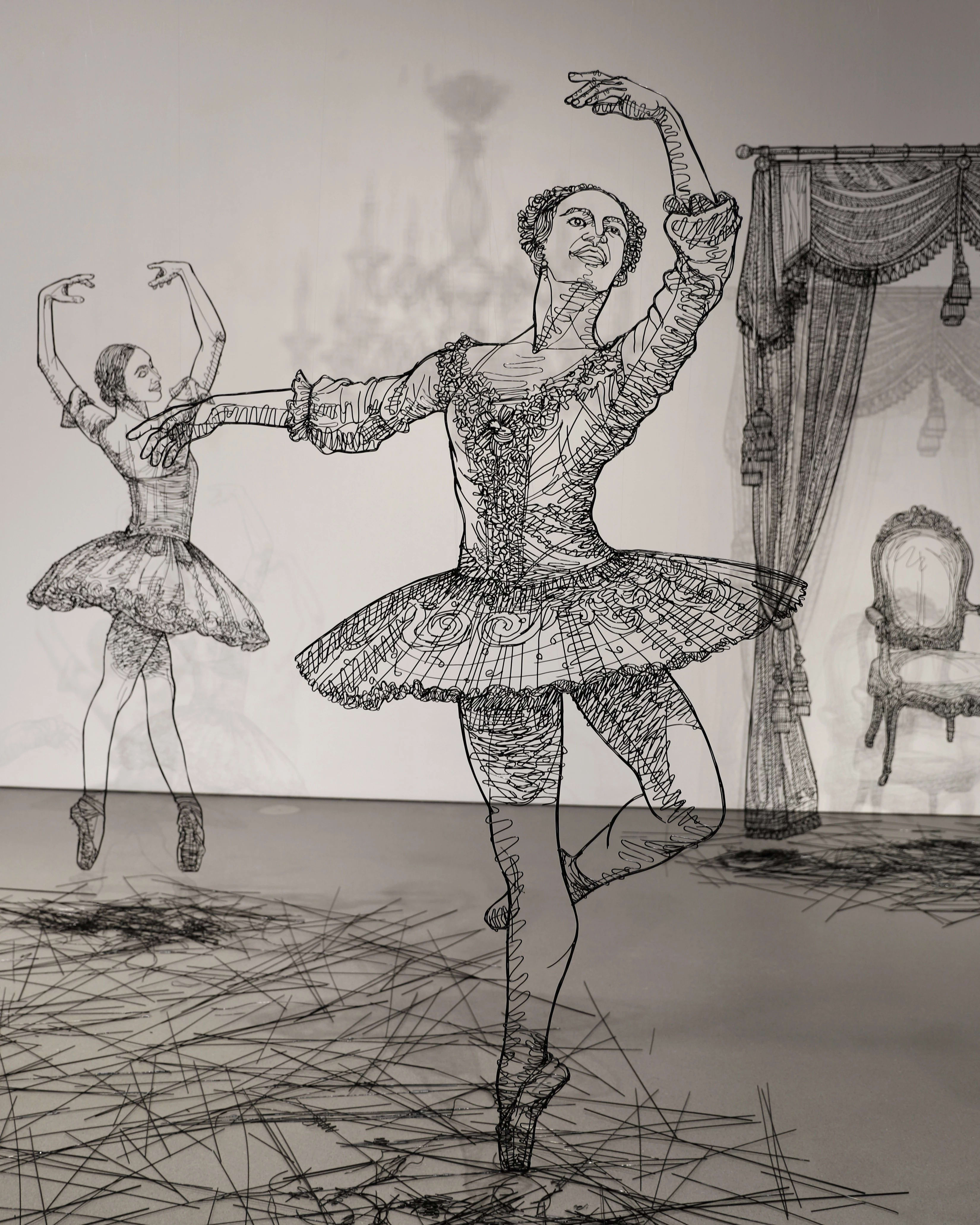 Close up of sculptures made in black wire of several large scale ballerinas dancing around a white room.