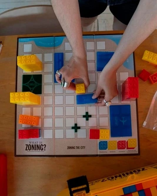 Hands placing Lego-type blocks on a grid-based game board.