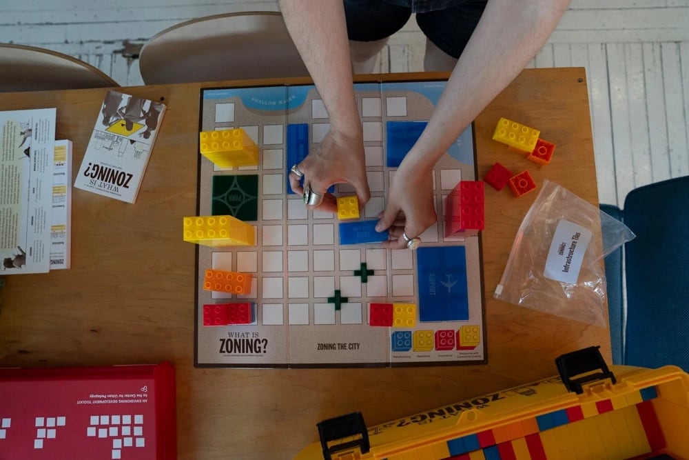 Hands placing Lego-type blocks on a grid-based game board.