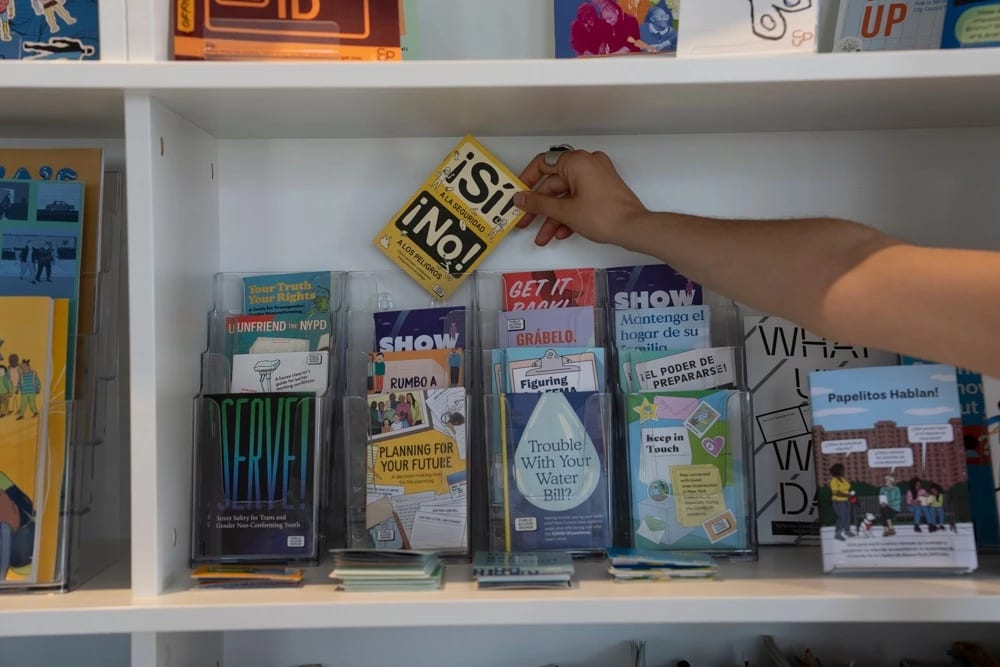 A photograph of a bookshelf that is holding a clear plastic display case filled with brochure-sized publications. Each publication is dedicated to a civic-education topic.