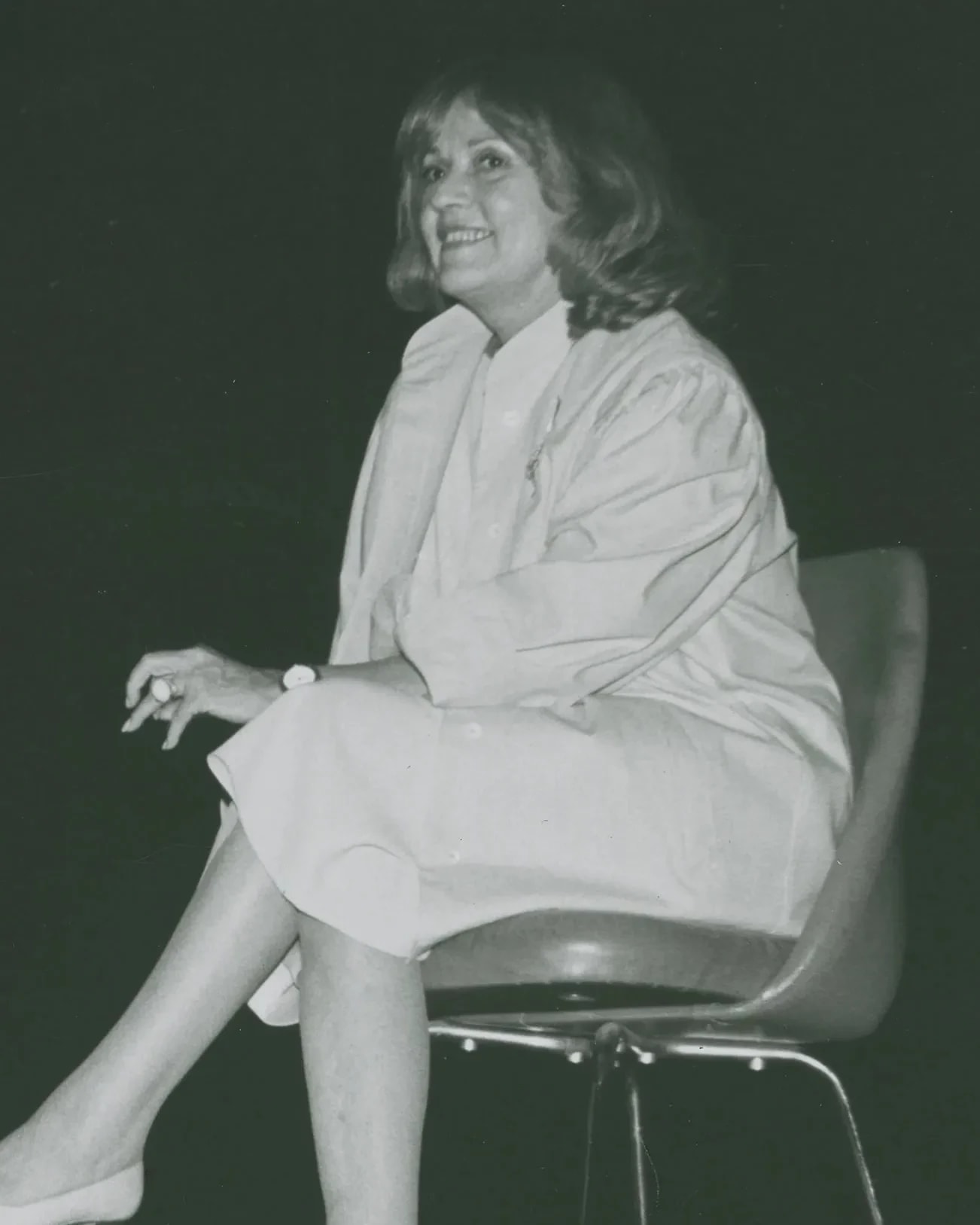 Two people sit in chairs on a stage in mid-discussion. The person on the left is pointing to something off-camera and both people are smiling.