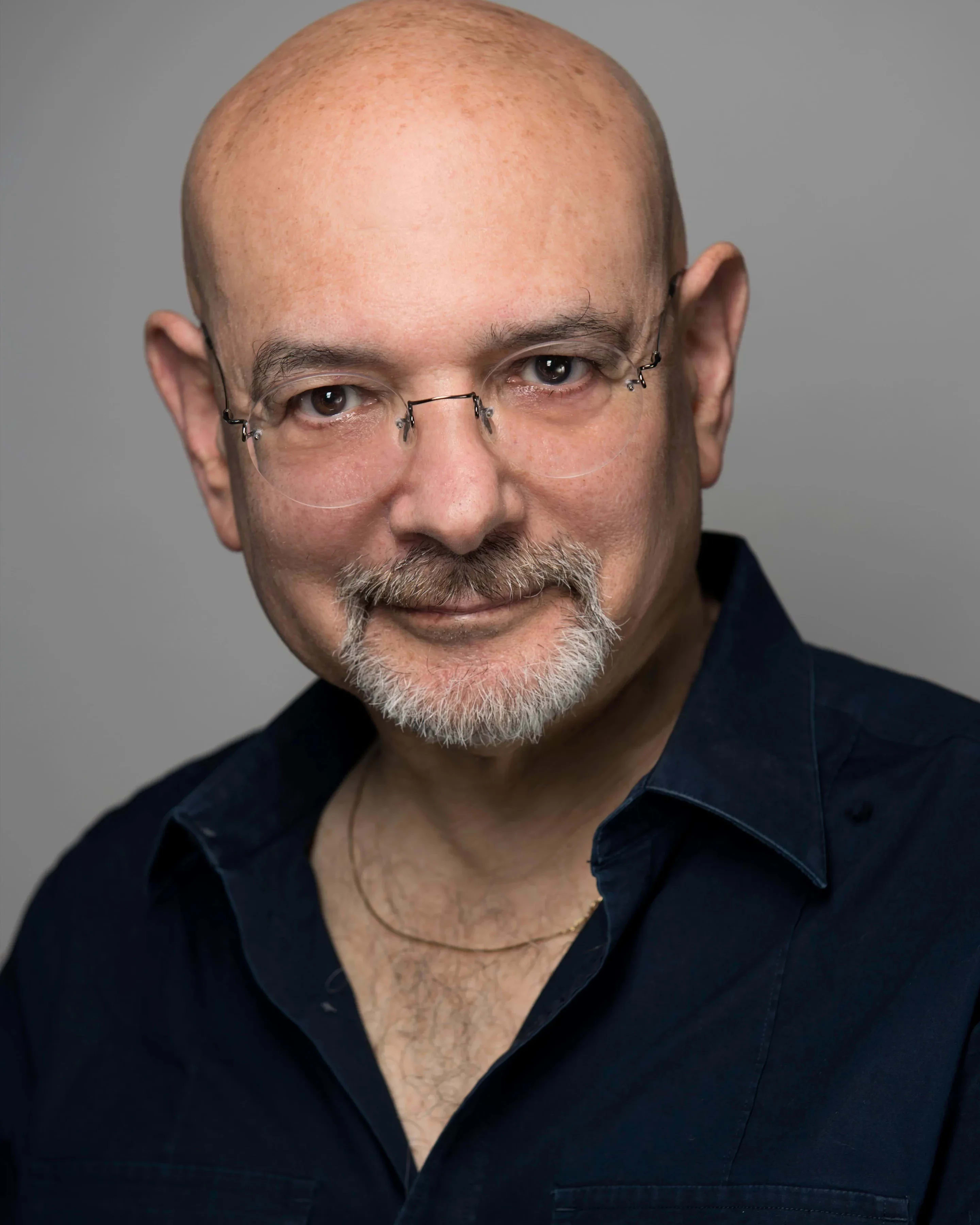 A white man with glasses and a goatee, wearing a dark shirt, poses against a plain background.