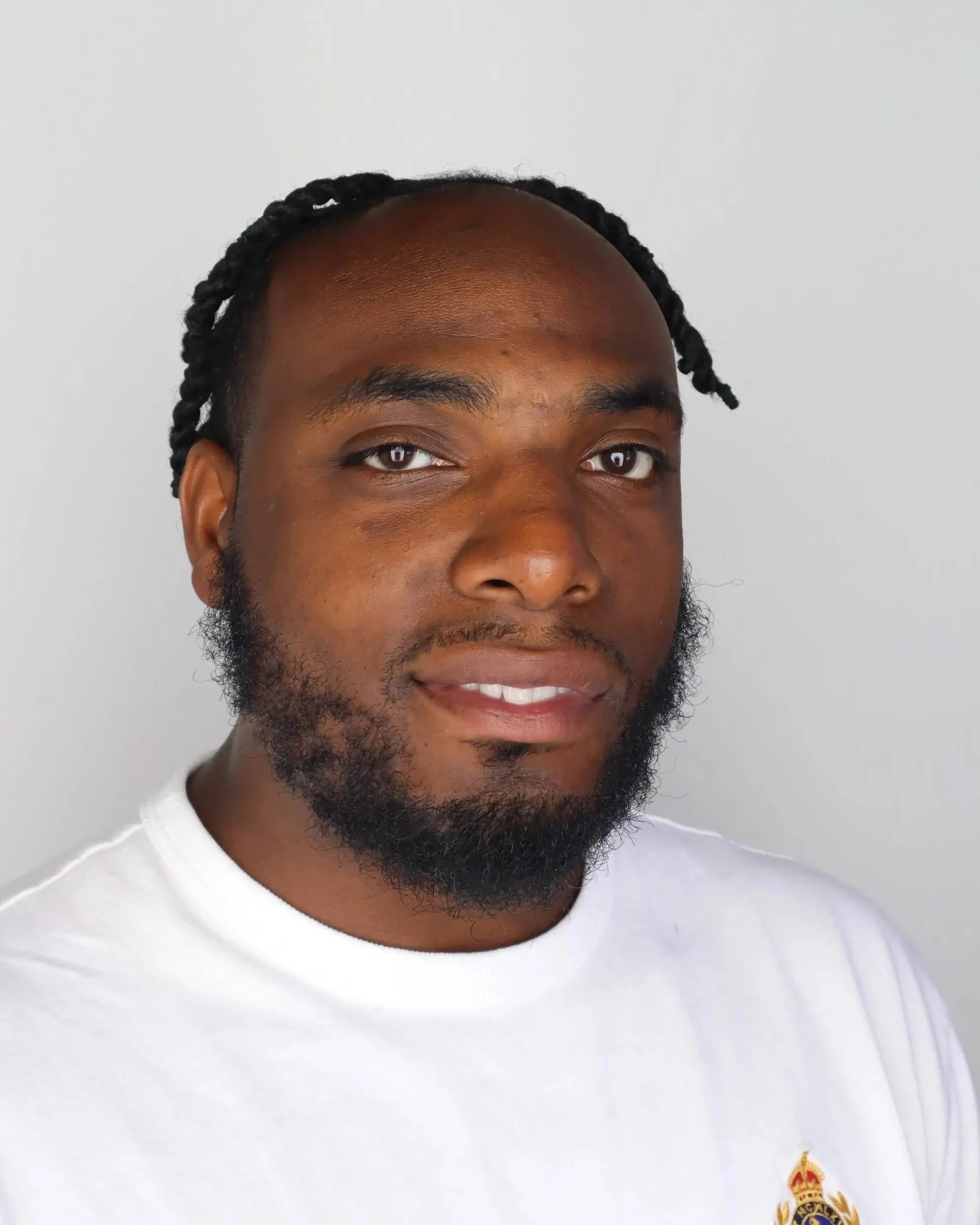 A man with a beard in a white t-shirt smiles and looks directly at the camera. 