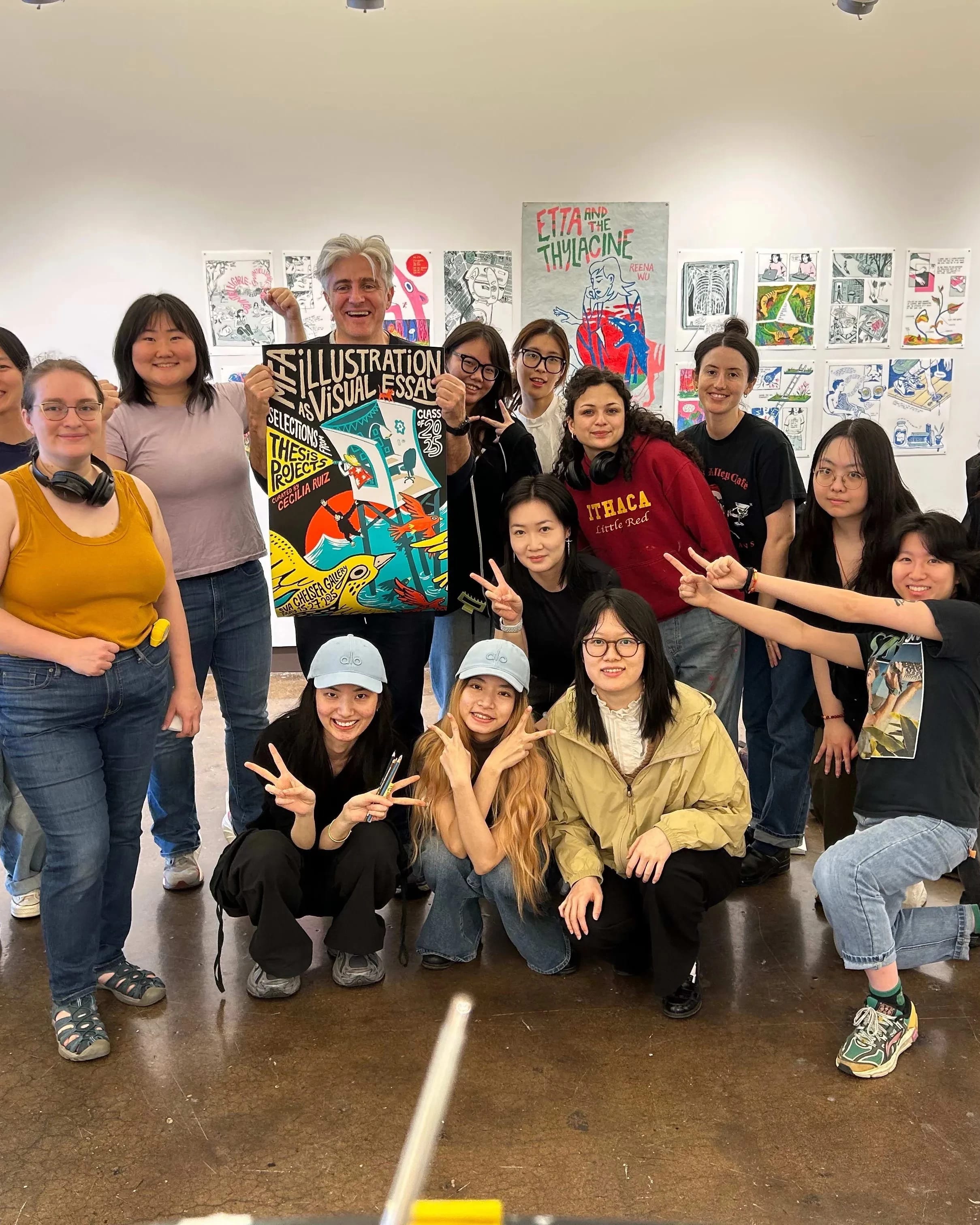 Students pose for a picture in a gallery with an instructor, who is showing off a poster design that they may have all worked on.