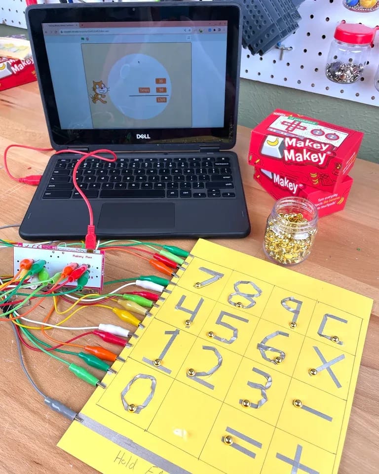 Two hands control a video game using pieces of playdough wired to a laptop.