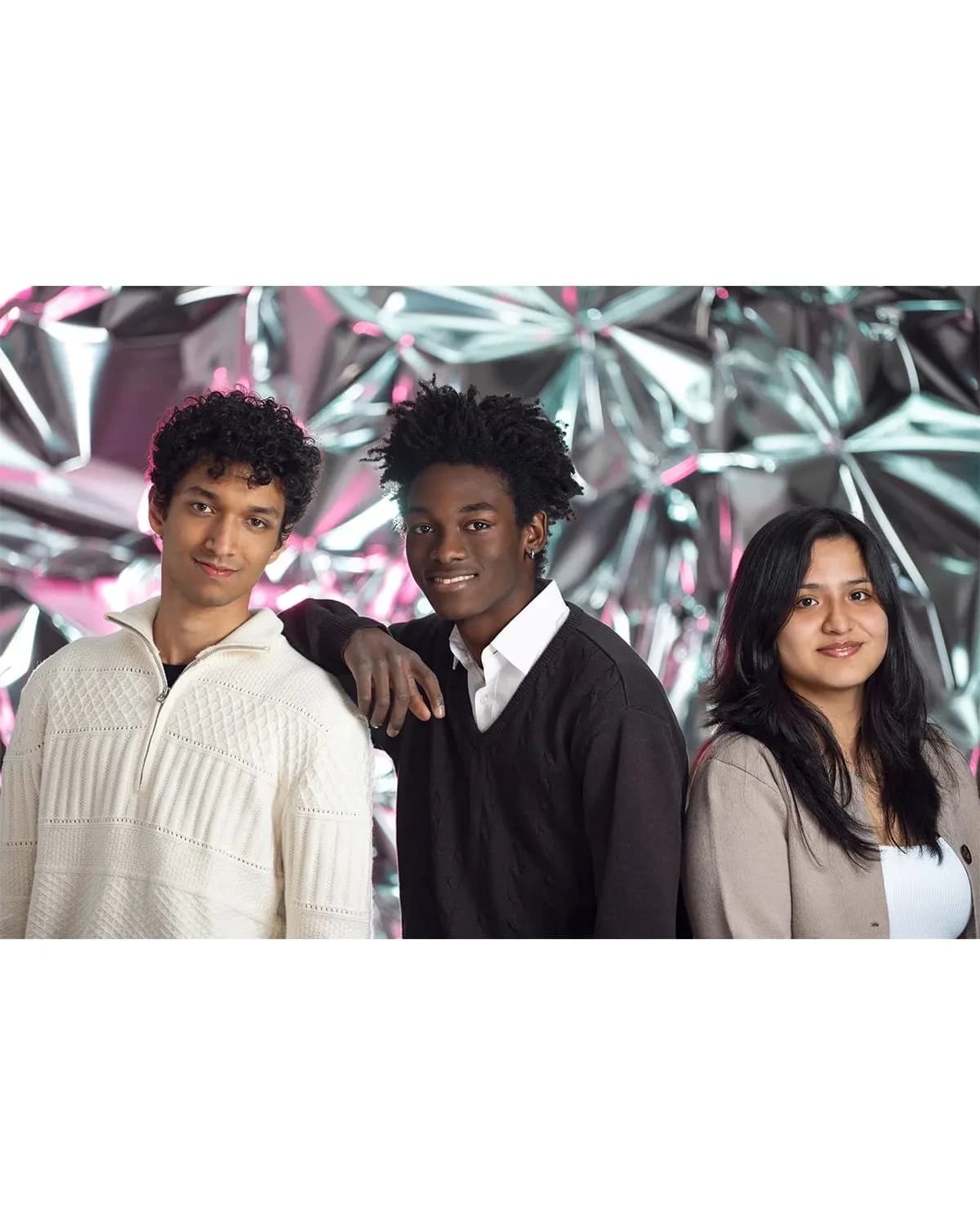 Two guys and a girl smile at the camera in front of a reflective background.