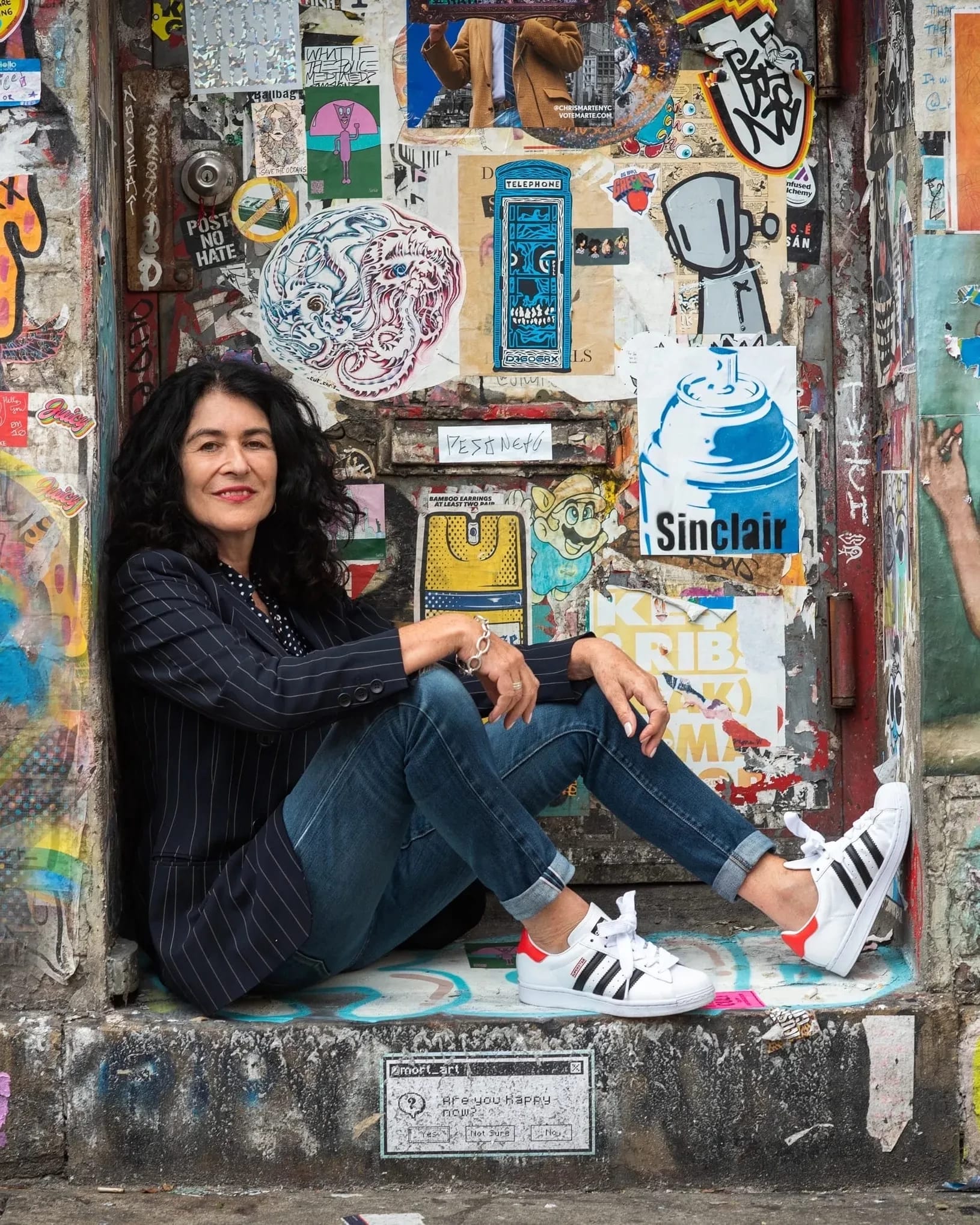 Portrait of photographer Janette Beckman sitting down in front of a graffiti-covered wall