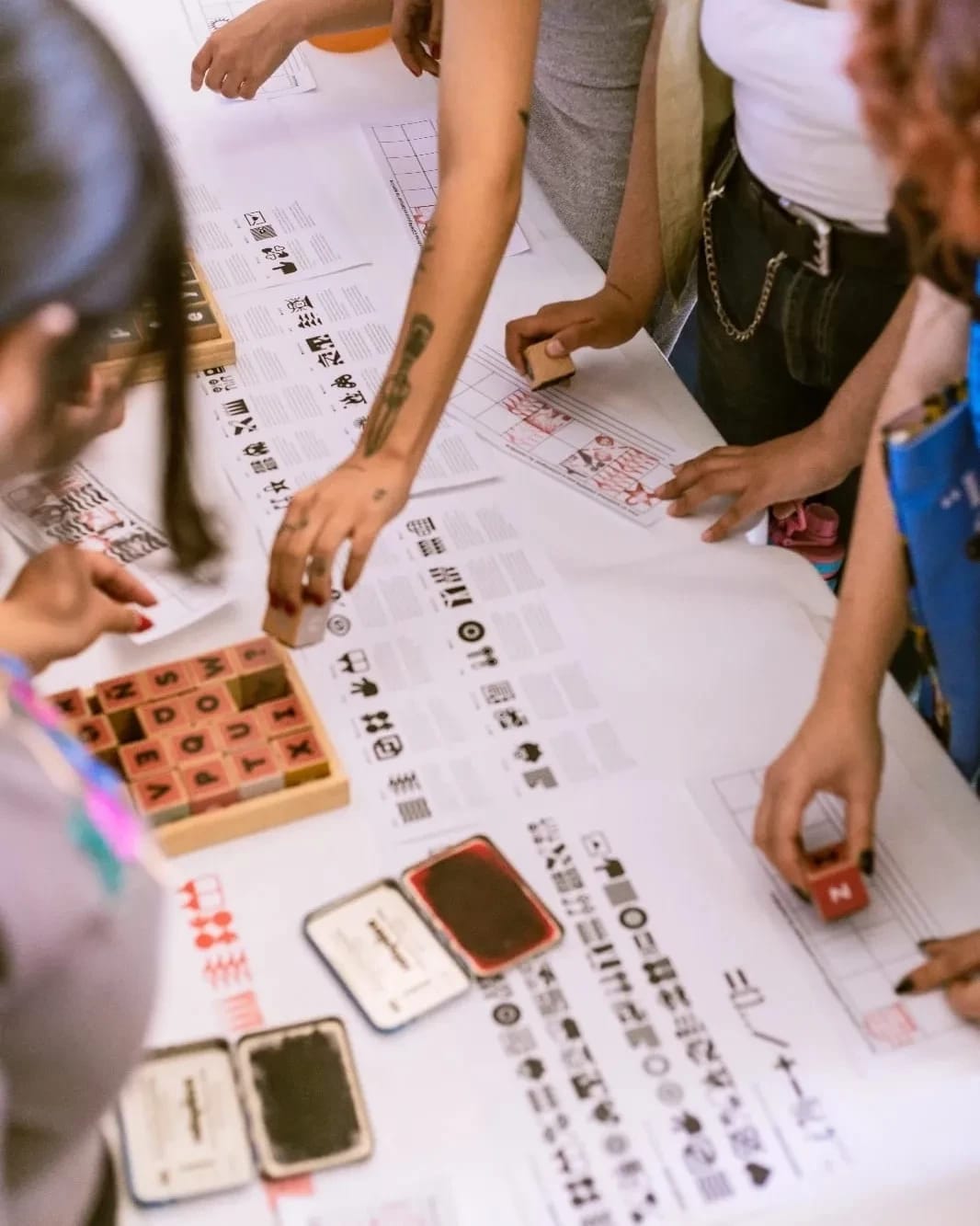 People gather around a table using wooden stamps on paper on a table.