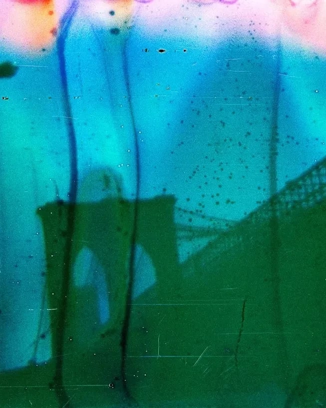 Abstract image of a bridge with an arch and cables, layered in vivid green, blue, and orange tones. The mood is surreal and dreamlike.