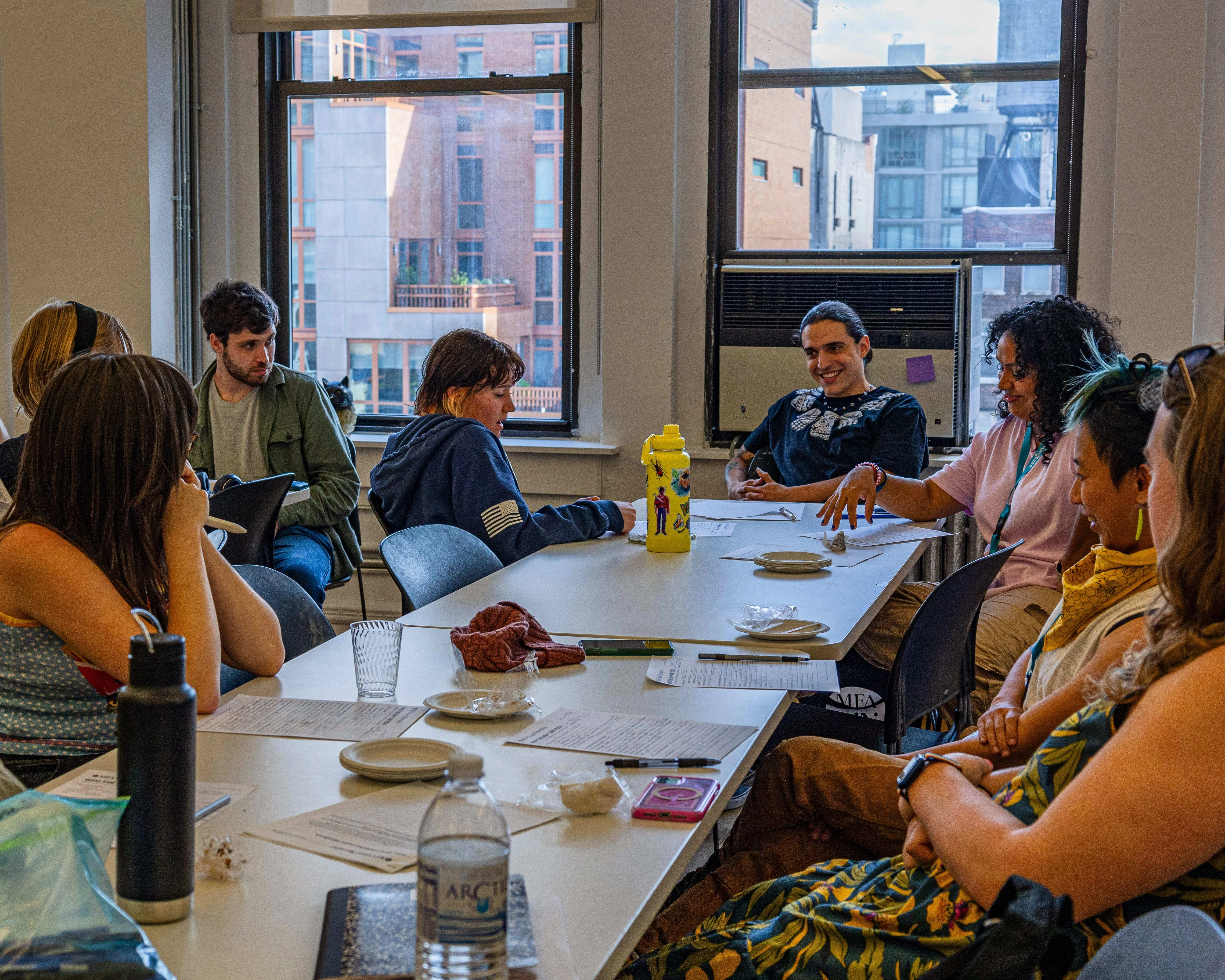 Photo of students sitting around a table in a classroom with windows.