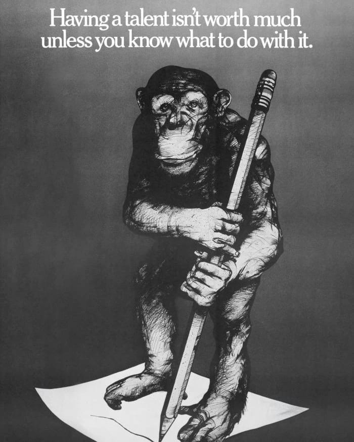 Black and white poster with a chimpanzee holding a large pencil while standing on a sheet of paper.
