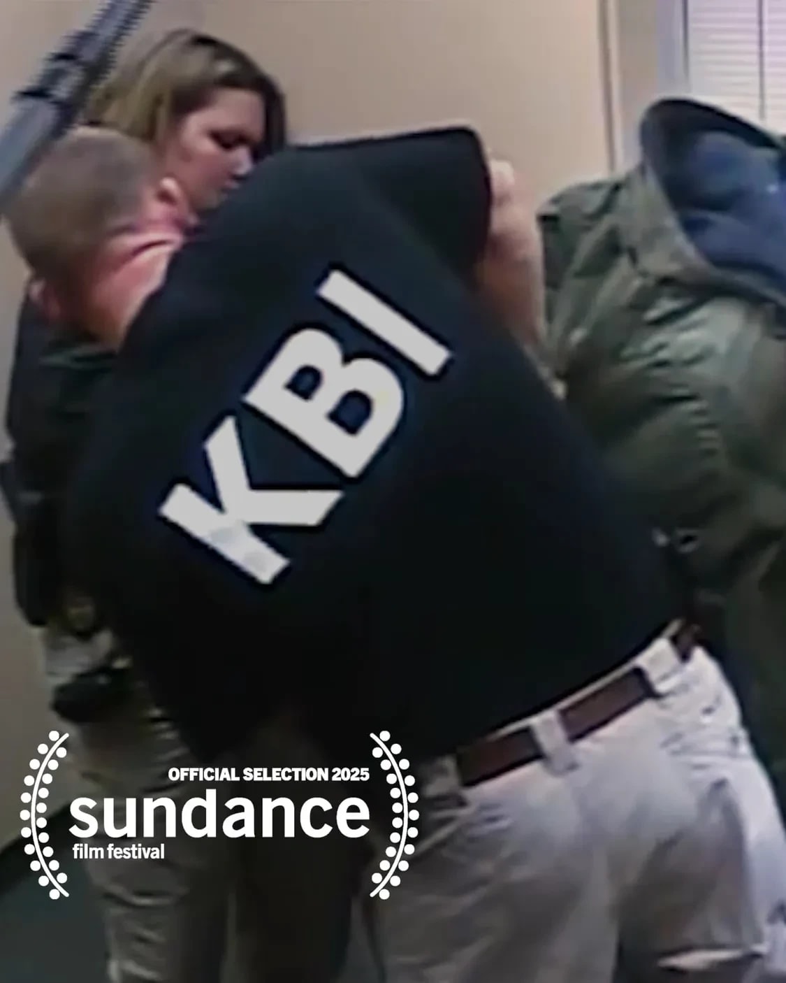 images of a man in a green jacket getting arrested by a man ion a black logo that says "KBI" on it. There's a third person who is. holding a big camera in the face of the man in the green jacket.