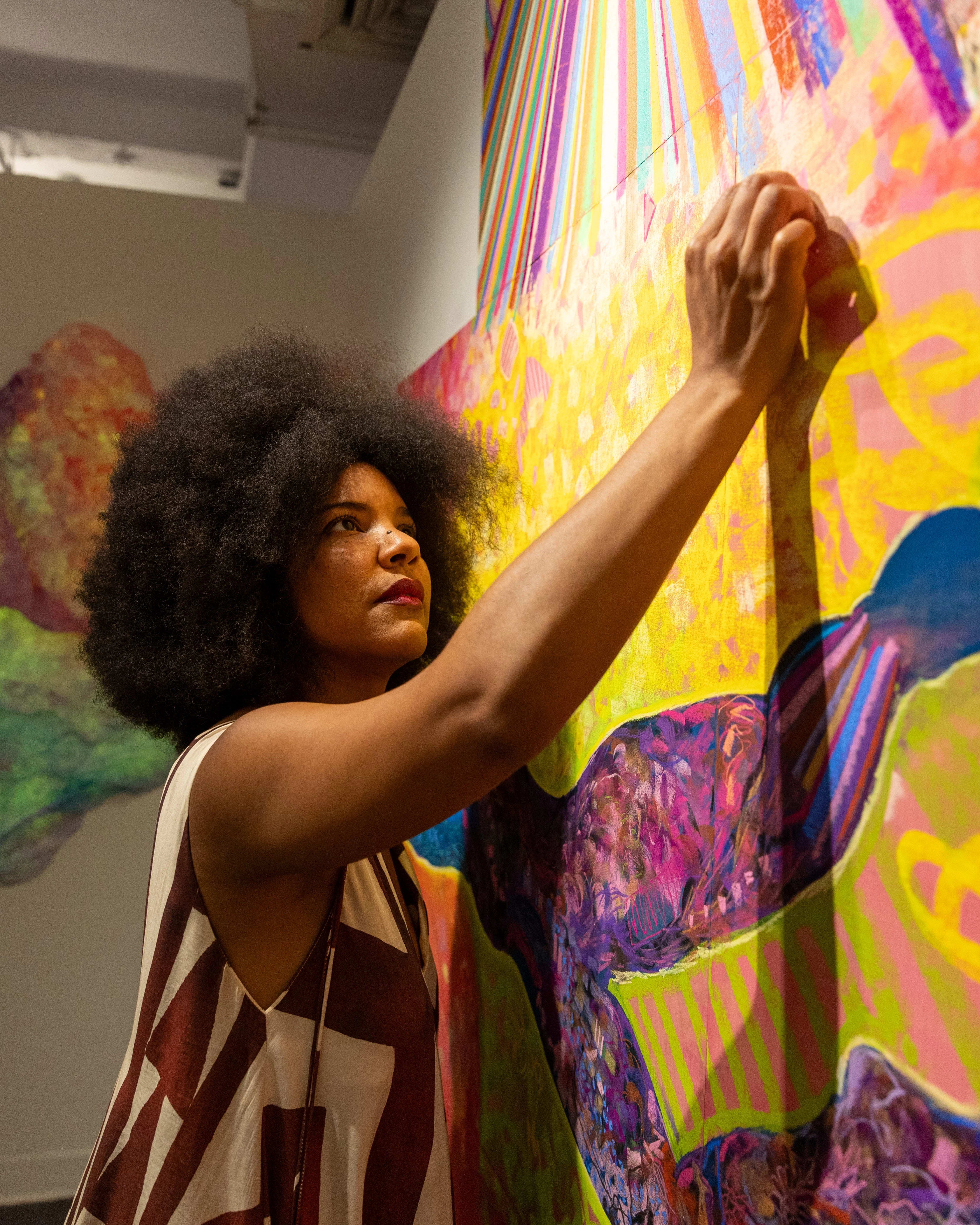 A woman draws in her studio wearing a colorful geometric brown and white tank top.