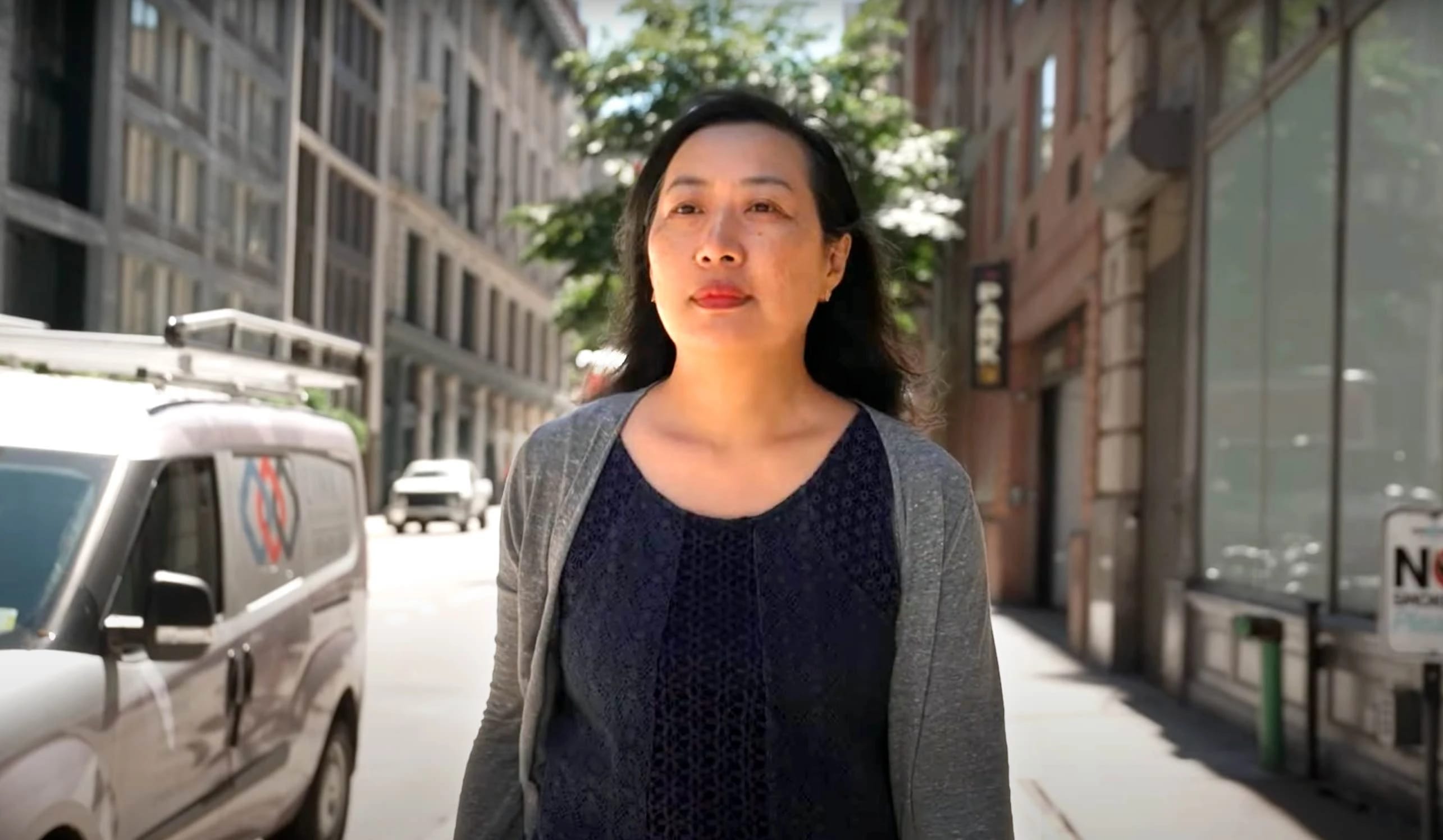 A woman wearing a blue shirt and gray sweater walks down a New York City street on the School of Visual Arts campus.