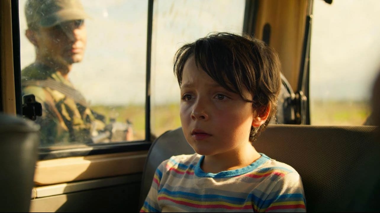  A young boy sitting in the back seat of a vehicle, looking out the window with a thoughtful expression.
