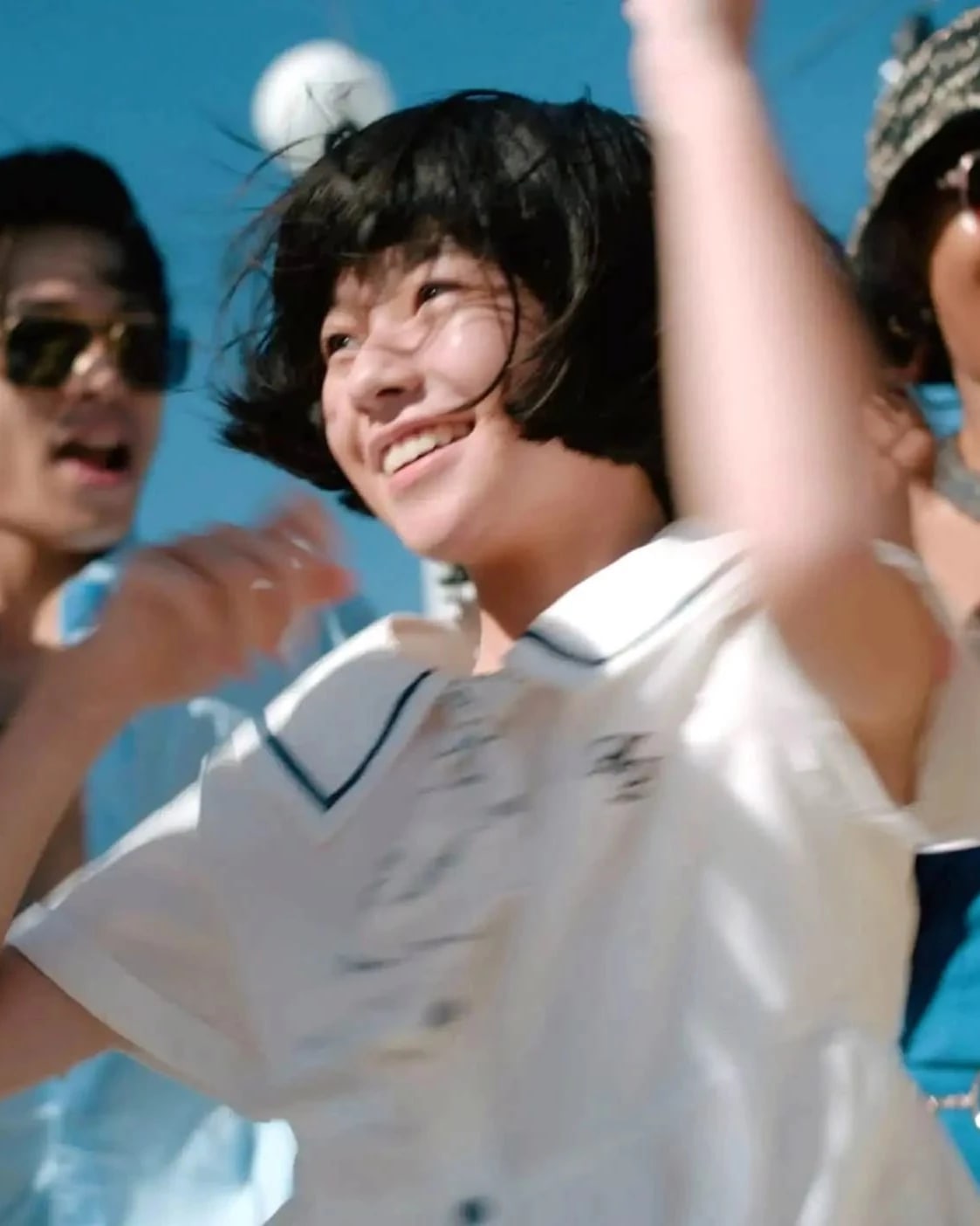 A joyful group of people dancing and smiling together under the bright sun.