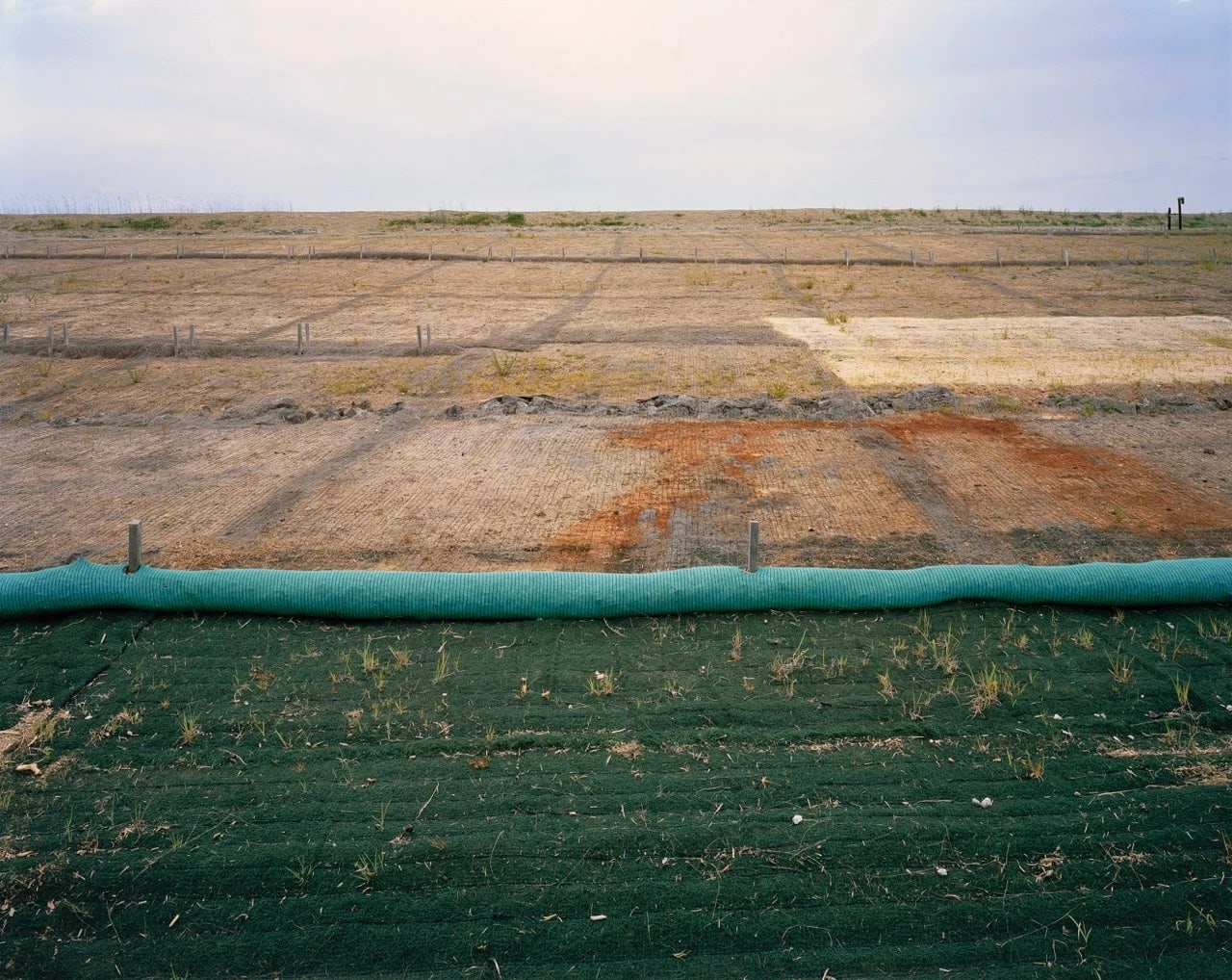 A photograph of a flat landscape, two-thirds of which is covered with brown grass and one-third of which is covered by a green fabric.