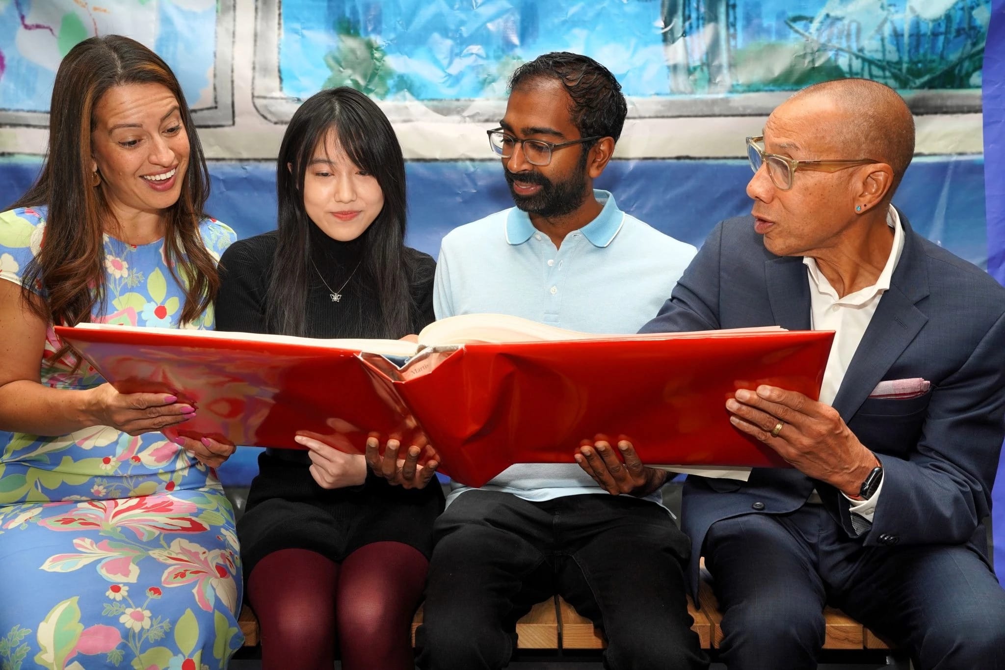 Two women and two men holding and looking at a large red book.
