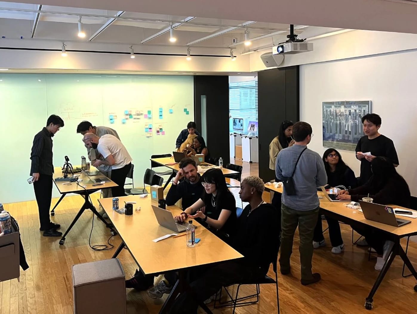 An open-plan workspace with several groups of two to four people gathered around different tables.