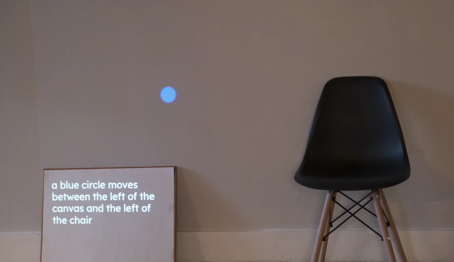 A black chair and white canvas next to a white wall. The Wall and canvas