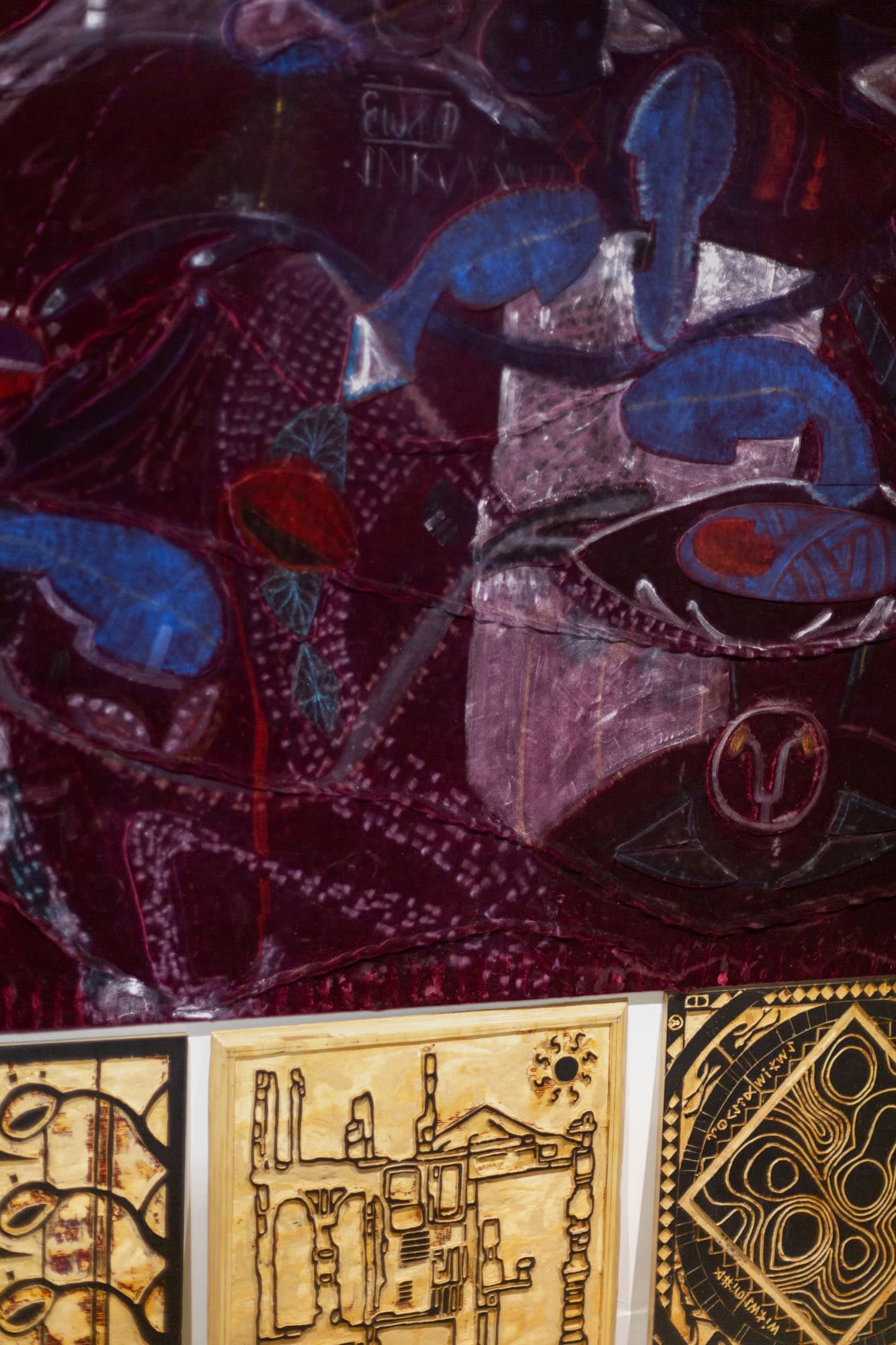 A detail of artworks by Sefa Ozdogan. The artwork on top is a painting of abstract shapes with different shades of blue, maroon, and white. The pieces on the bottom are made of carved wood with areas painted in black.