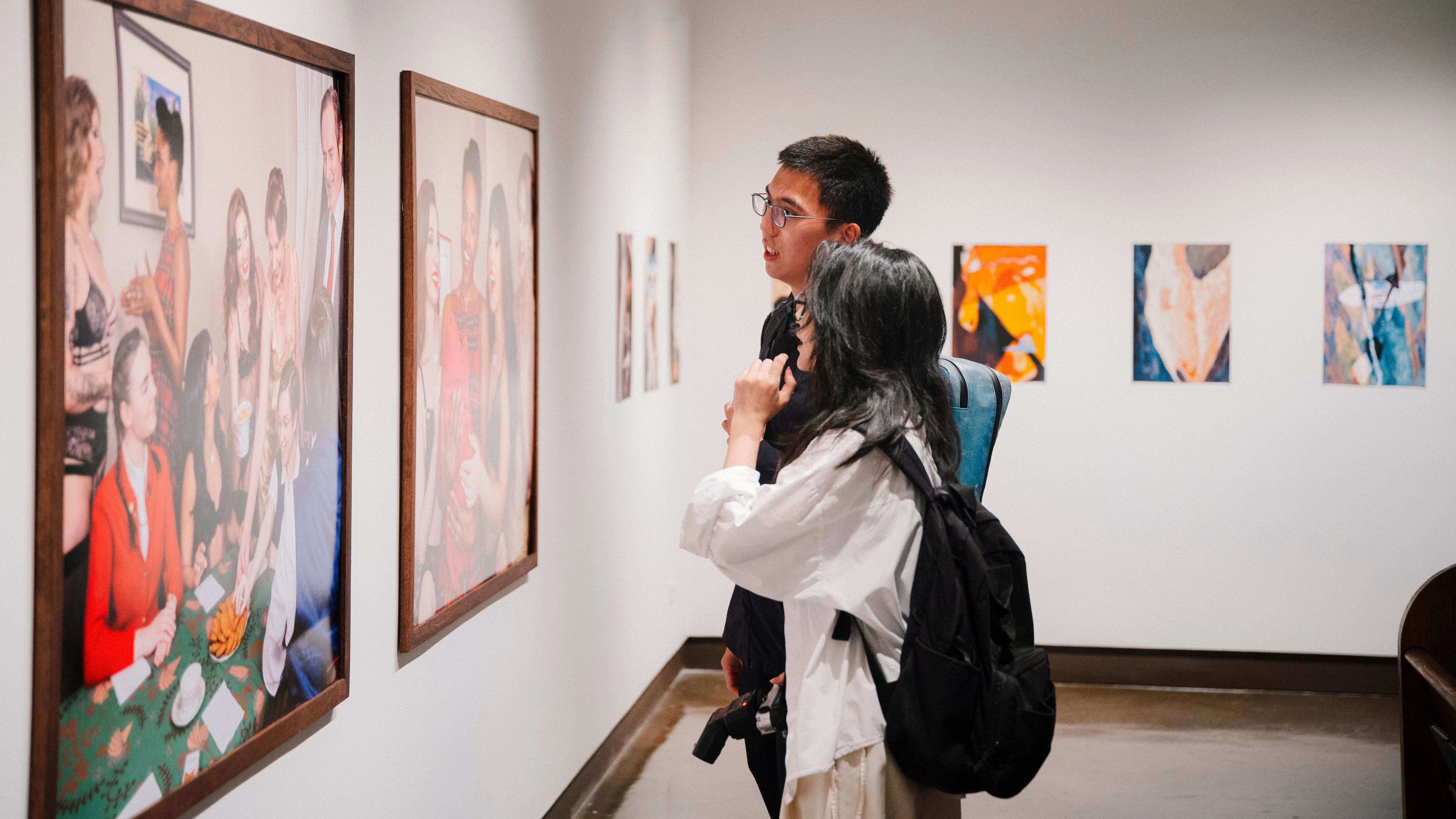 An image of two people standing in front of a gallery wall looking at a photograph.