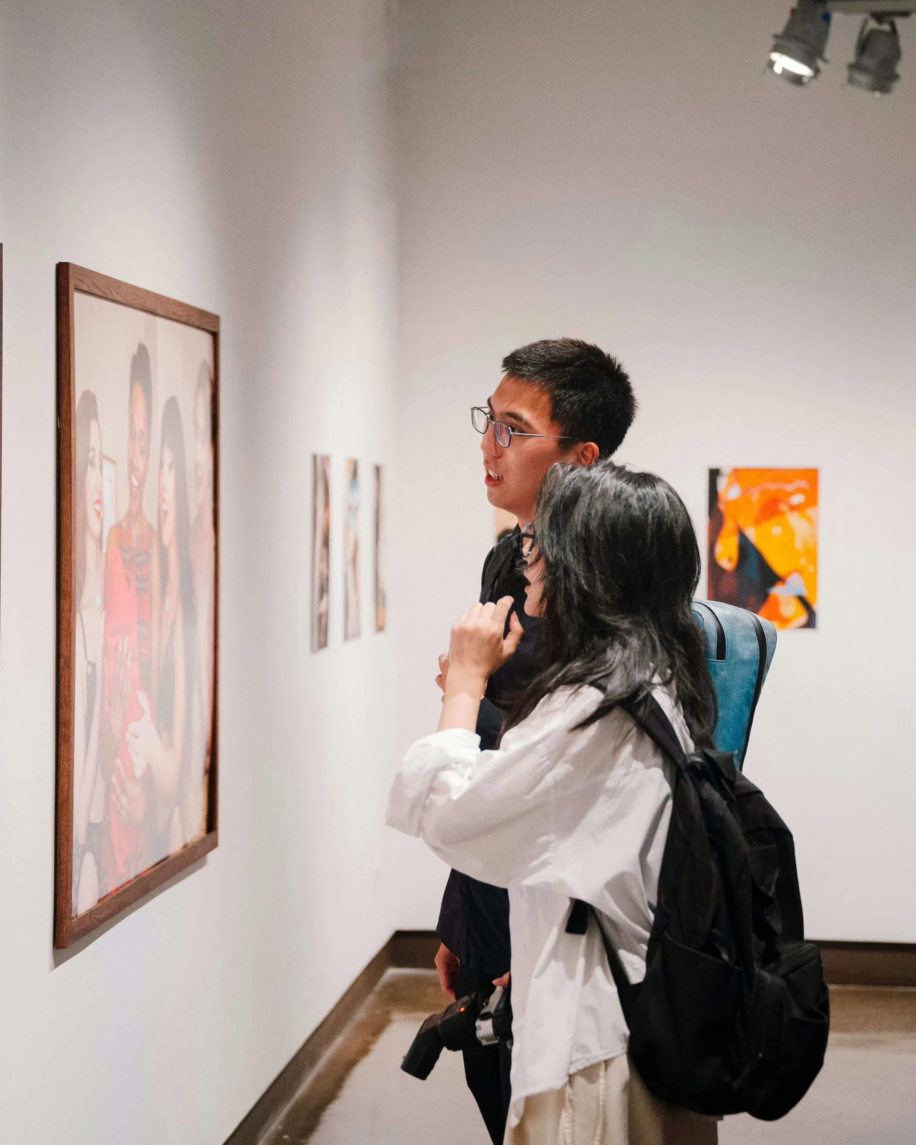 An image of two people standing in front of a gallery wall looking at a photograph.
