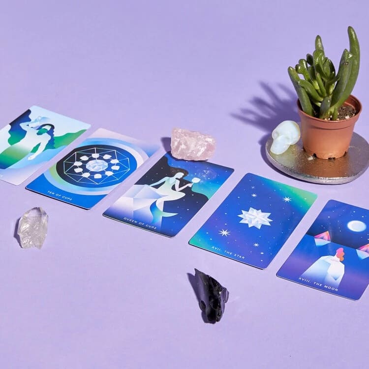 Cool colored tarot cards are on a purple surface. There are a few crystals and a potted succulent as well.