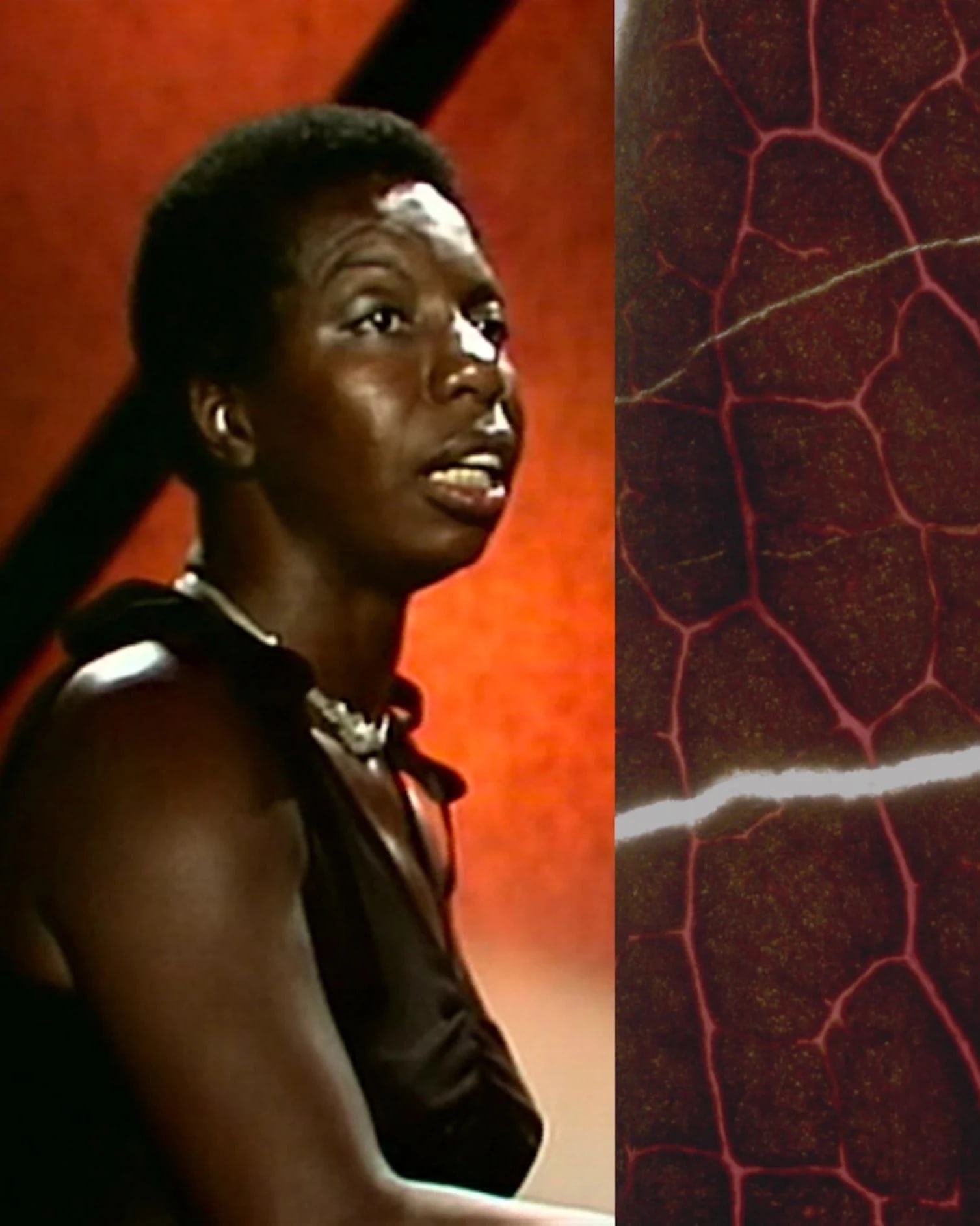 Video still of a woman looking off camera, sitting in an environment mostly composed of deep red tones.