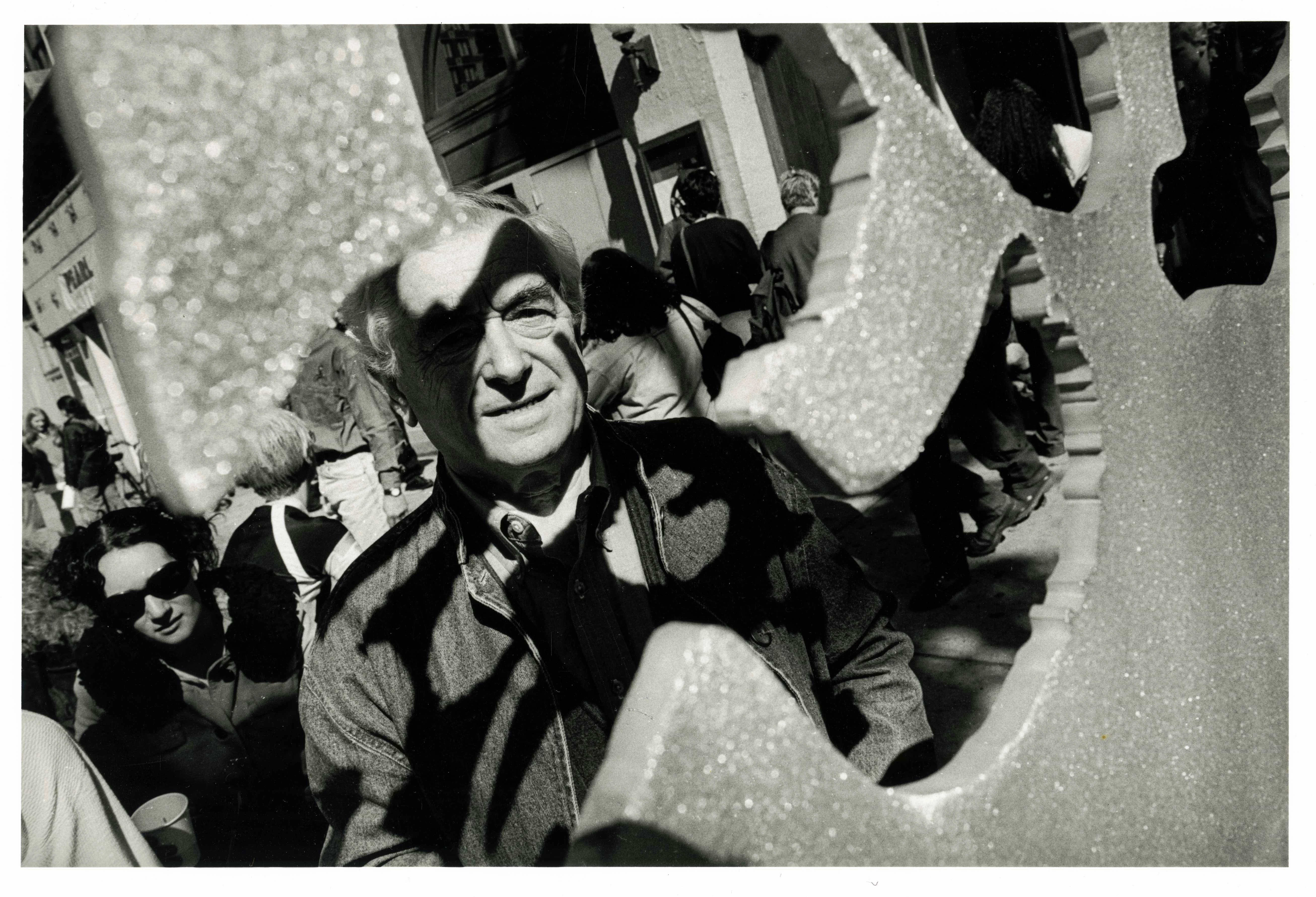 A black and white image of a man, silhouettes falling onto his face standing in front of an abstract flower sculpture.