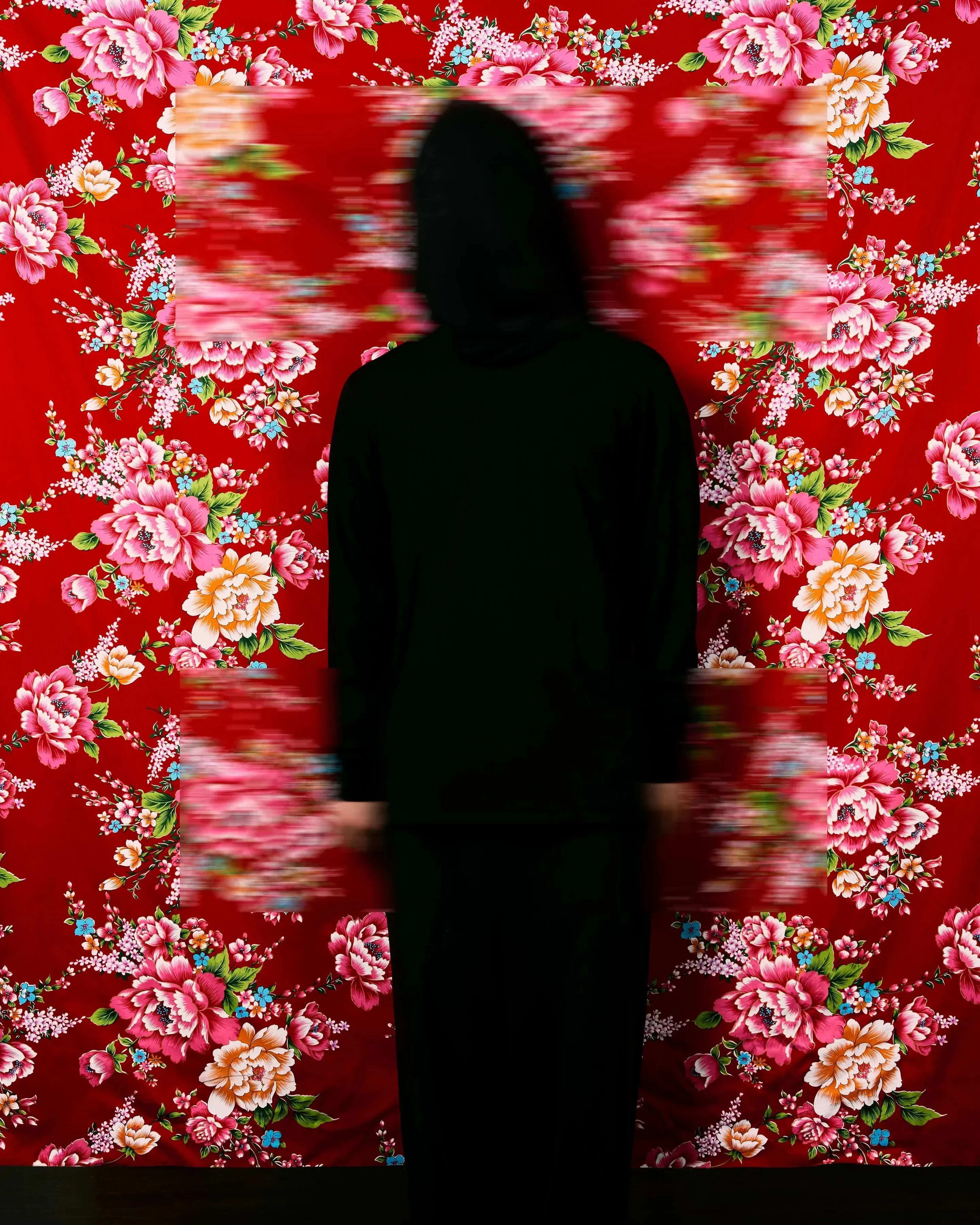 A black silhouette stands in front of a bright red floral wallpaper with two rectangular patches blurred.